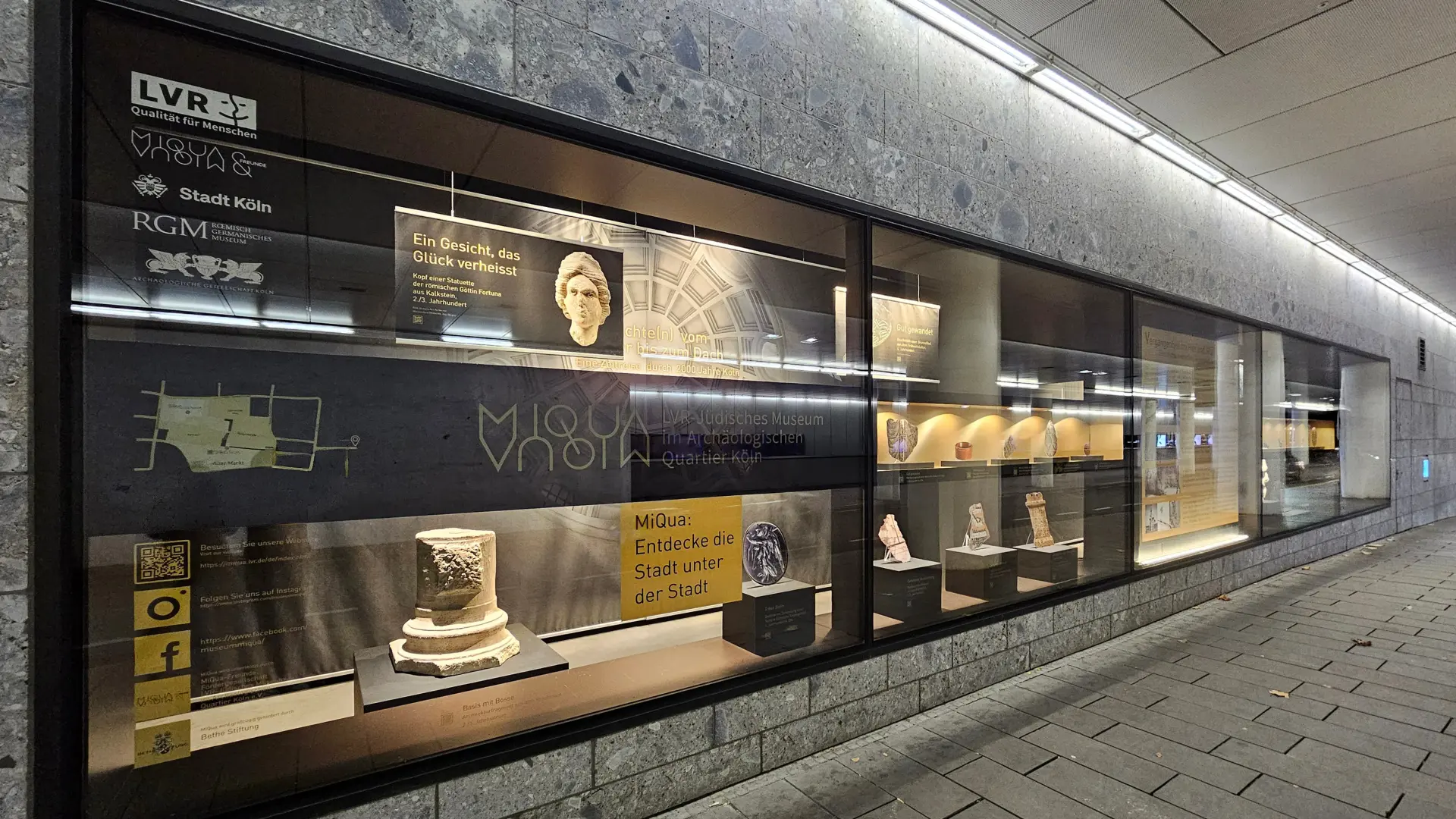 Das Logo des Museum MiQua auf einem schwarzen Bauzaun.