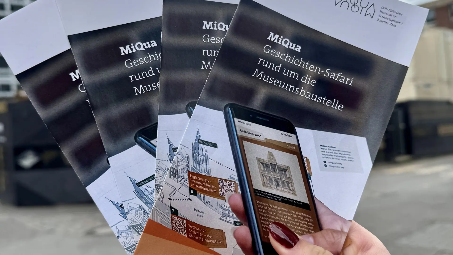 Eine Hand hält mehrere Flyer der Geschichten-Safari hoch.