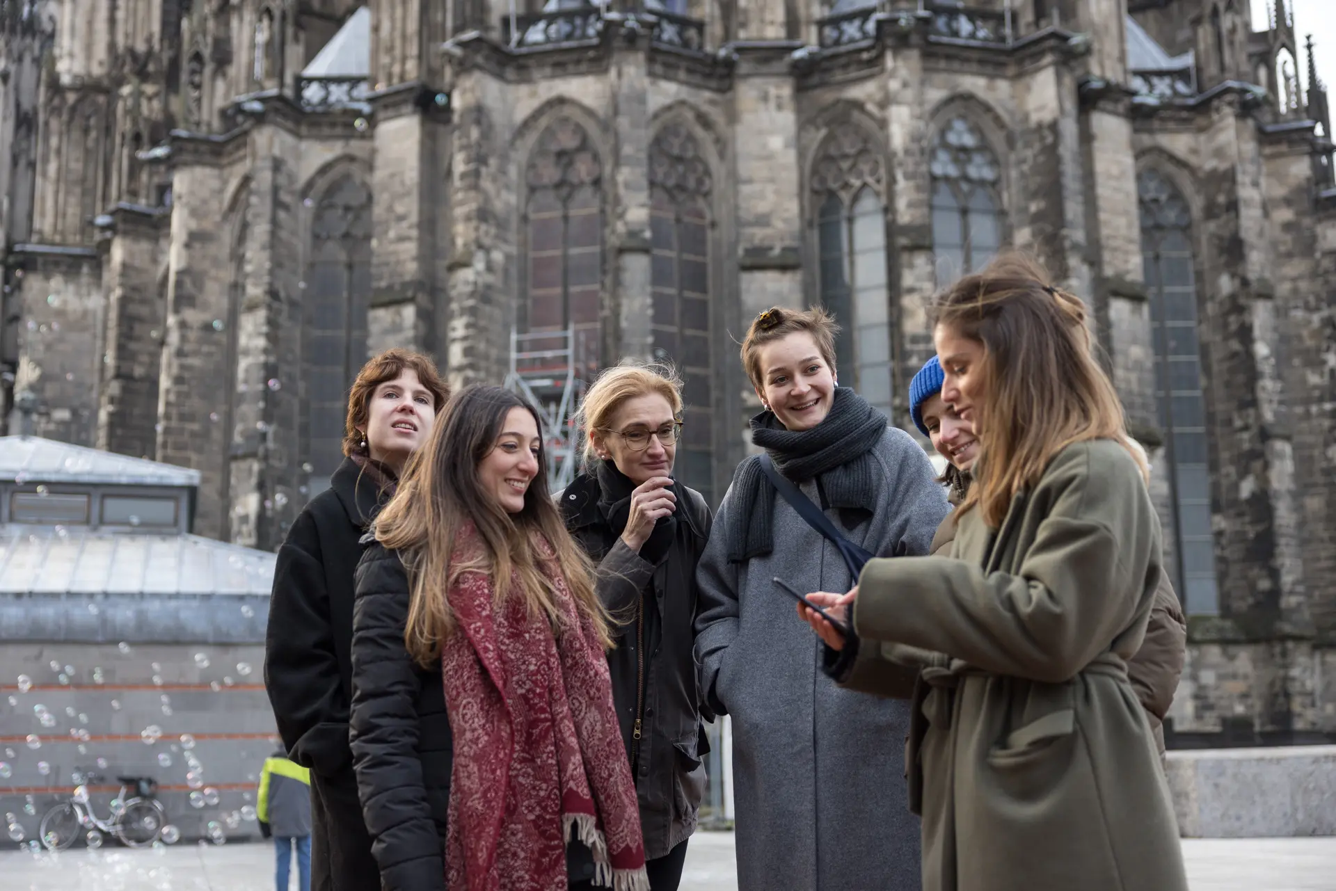 Ein Gruppe Menschen steht vor einem Gebäude mit einer dunklen Steinfassade.  Sie schauen gemeinsam auf einen Stadtplan.