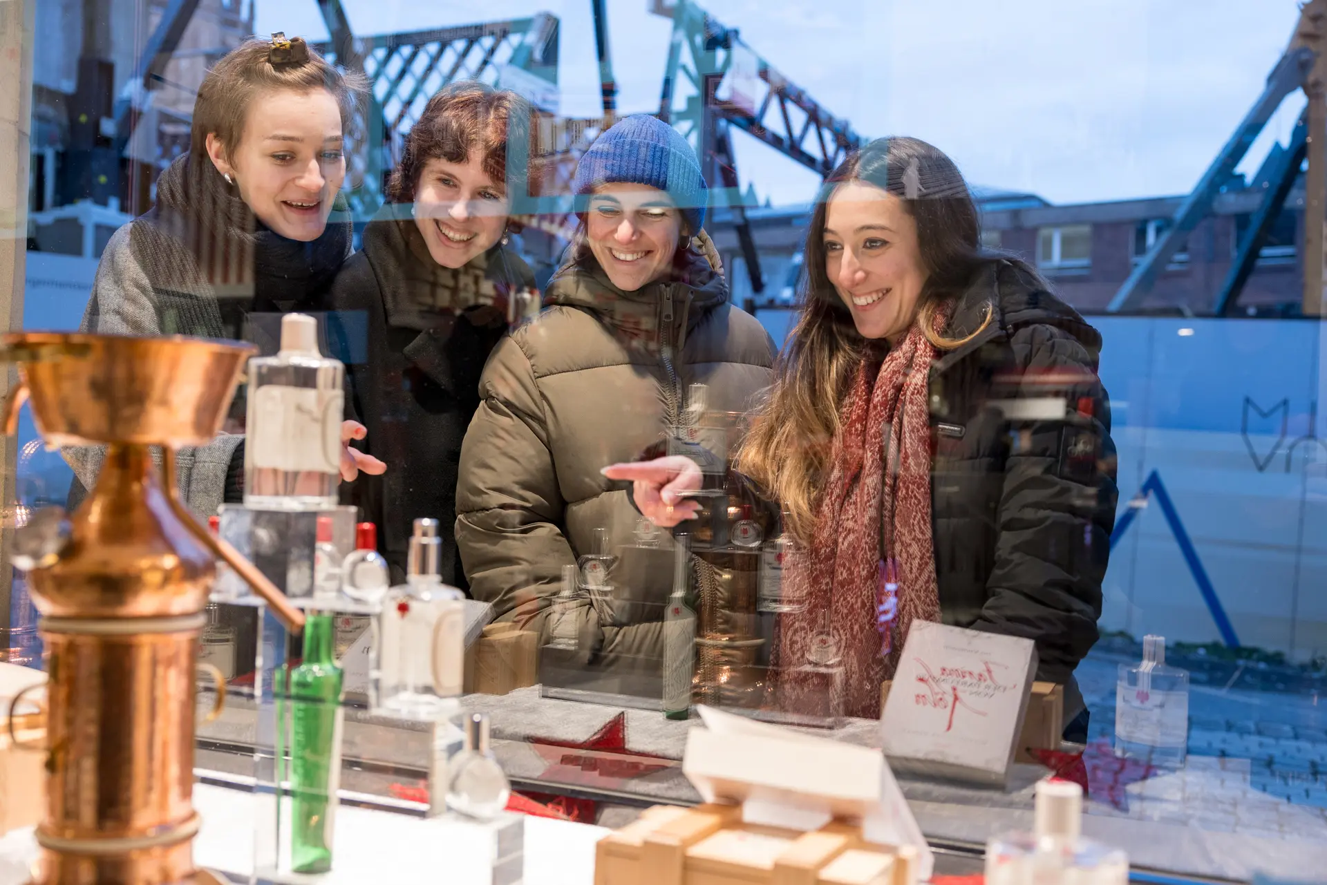 Eine Gruppe von Frauen schaut durch ein Schaufenster das kleine Parfümfläschen enthällt.