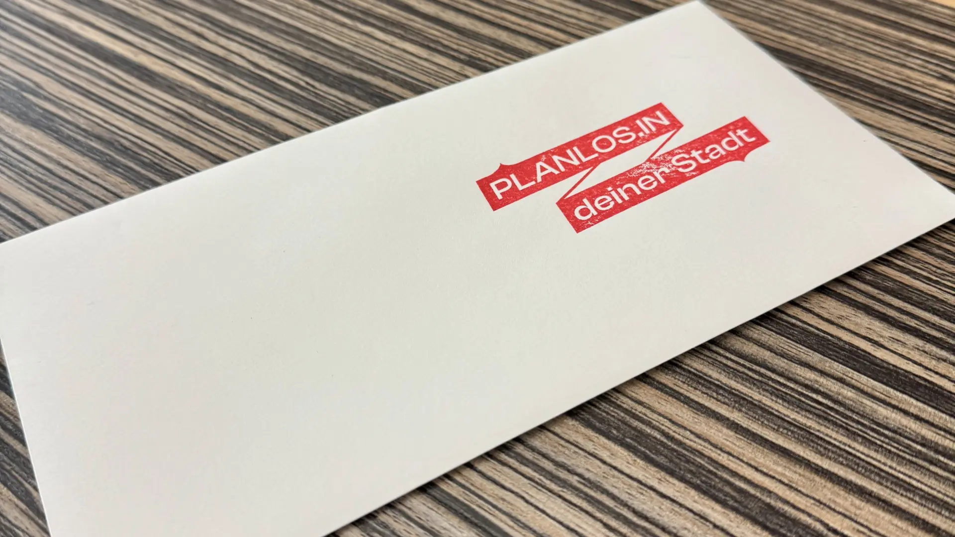 Eine Hand hält ein Handy.  Im Hintergrund sieht man eine Steinmauer, auf der eine goldene Plakette befestigt ist.