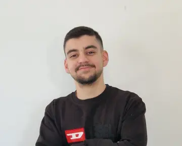 Ein junger Mann mit schwarzem Oberteil lächelt in die Kamera.