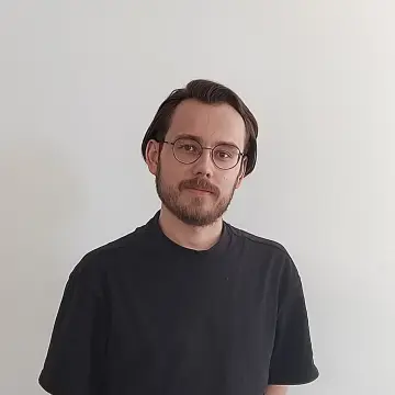 Bild: Ein junger Mann in schwarzem T-Shirt lächelt in die Kamera.