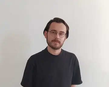 Bild: Ein junger Mann in schwarzem T-Shirt lächelt in die Kamera.