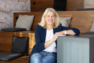 Bild: Eine Frau mit langen Haaren sitzt auf einer Treppe und lächelt in die Kamera.