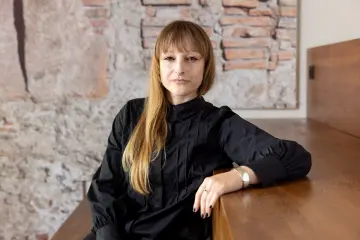 Eine Frau mit langen Haaren sitzt auf einer Treppe und lächelt in die Kamera.