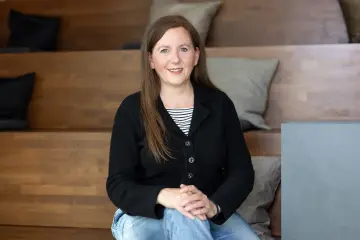 Eine Frau mit langen Haaren sitzt auf einer Treppe und lächelt in die Kamera.
