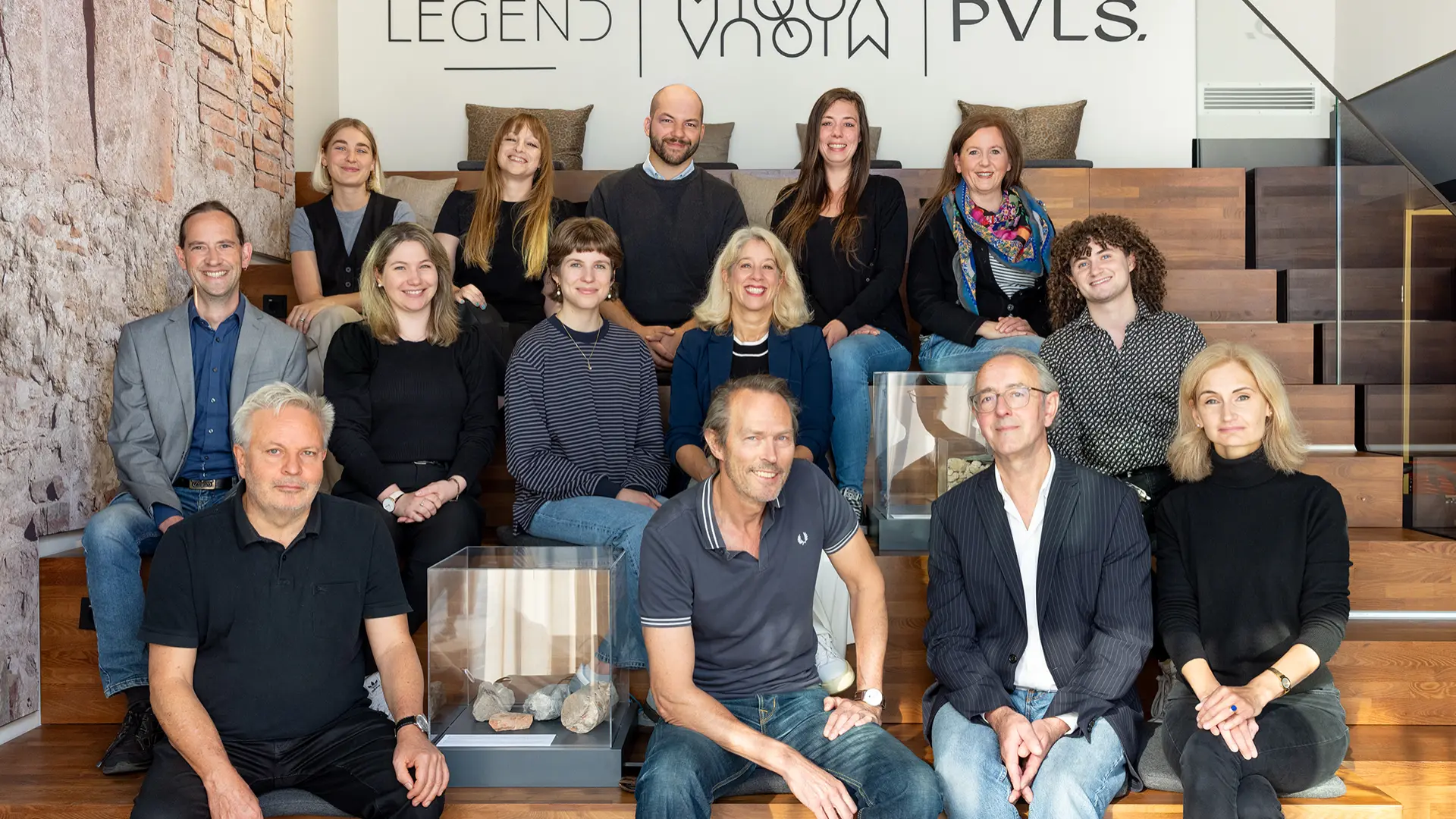 Eine Gruppe von Frauen und Männern sitzt auf einer Treppe und lächeln in die Kamera.