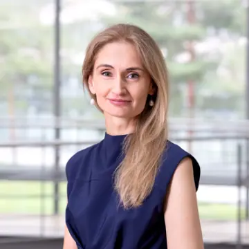 Eine Frau mit langen braunen Haaren, die über ihrer linken Schulter liegen, lächelt in die Kamera.