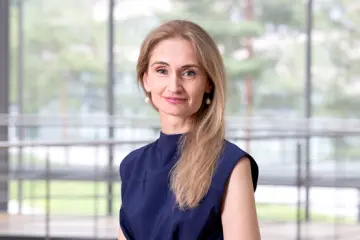 Eine Frau mit langen braunen Haaren, die über ihrer linken Schulter liegen, lächelt in die Kamera.