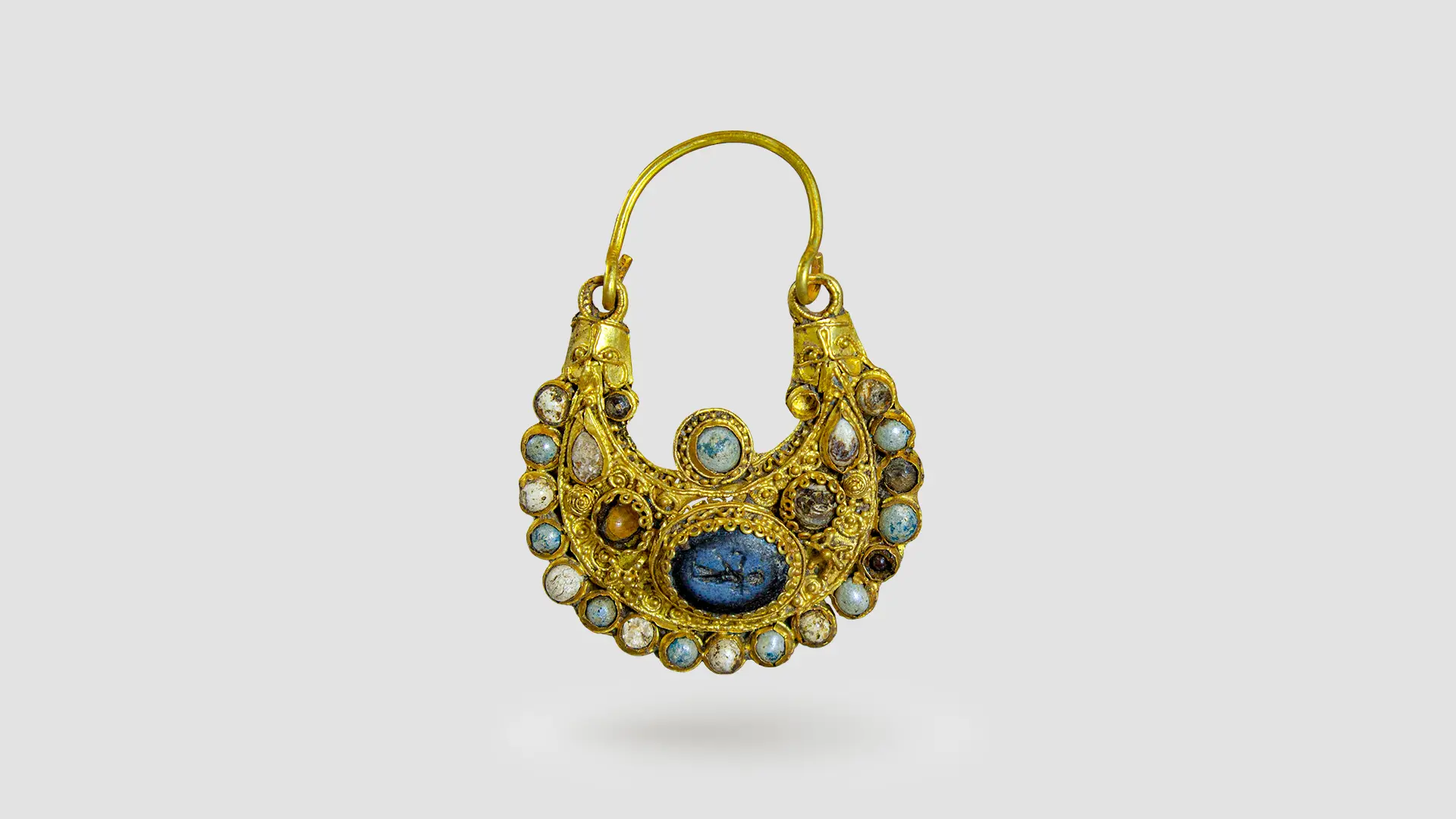 Ein goldener Ohrring der mit bunten Edelsteinen besetzt ist.