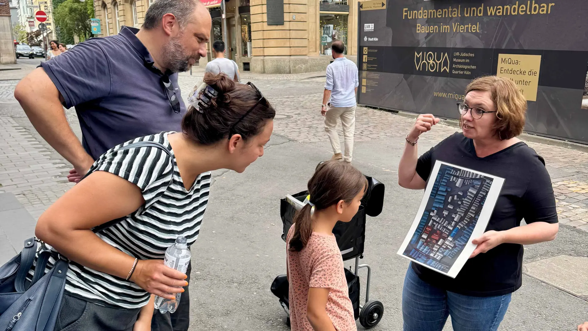 Eine Stadtführerin zeigt einer Familie eine Zeichnung.