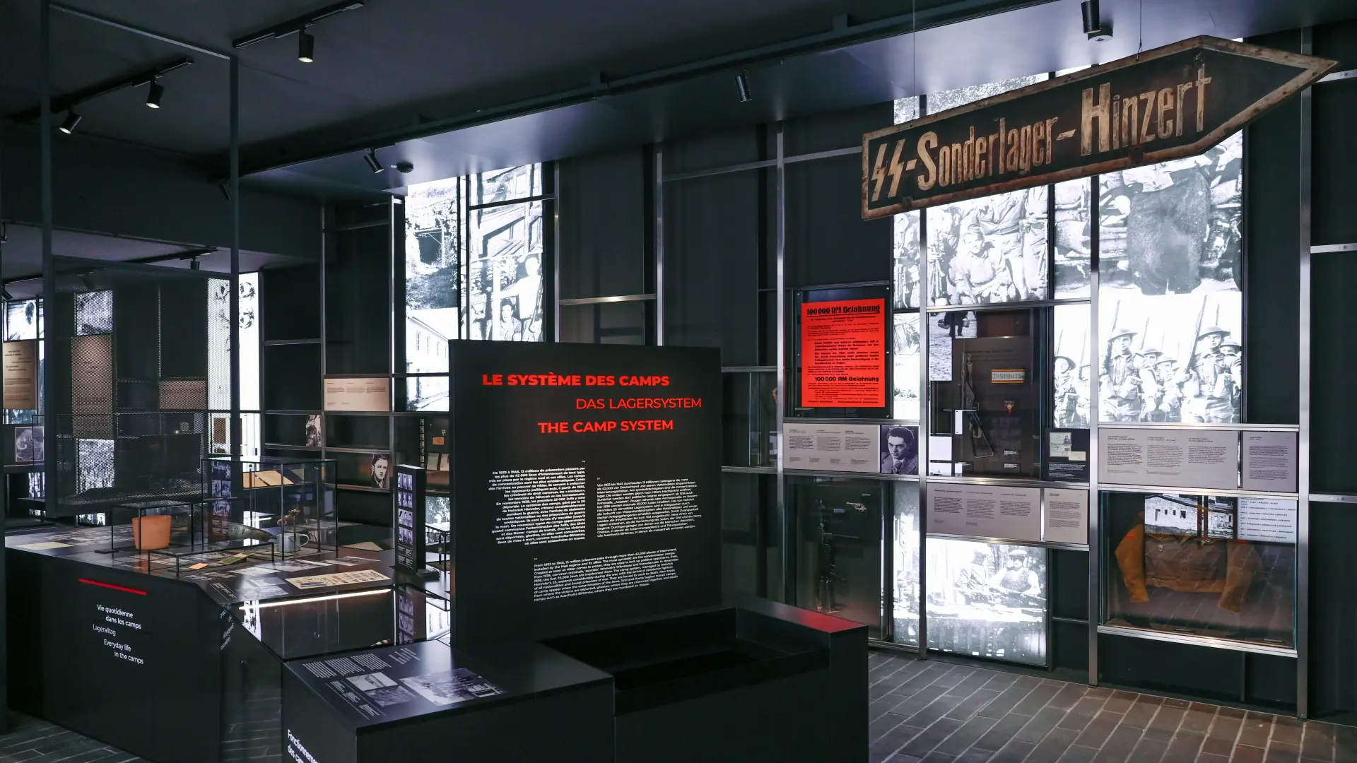Ein Blick in einen dunklen Museumsraum wo verschiede digitale Anzeigen in schwarz-weiß und rot zu sehen sind.