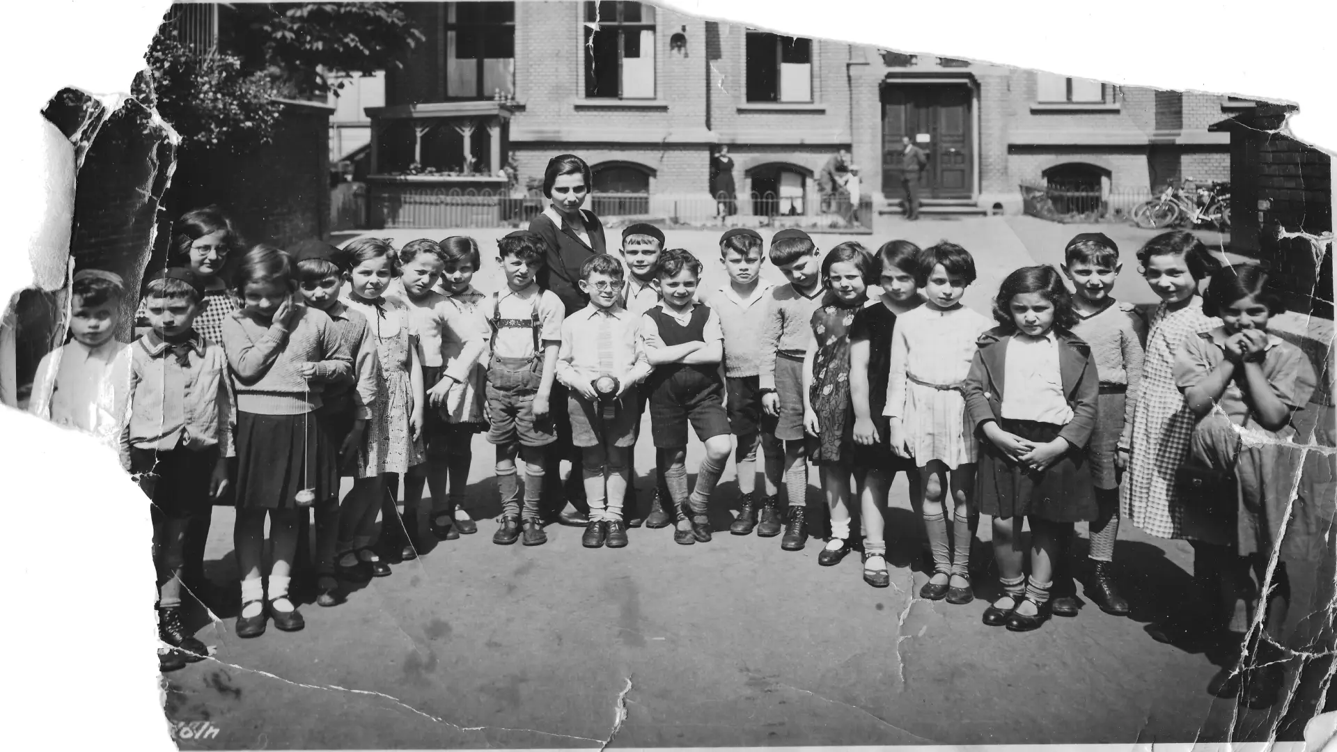 Ein schwarz-weiß Foto einer Schulklasse aus jungen Mädchen und Jungen vor einem historischen Gebäude.