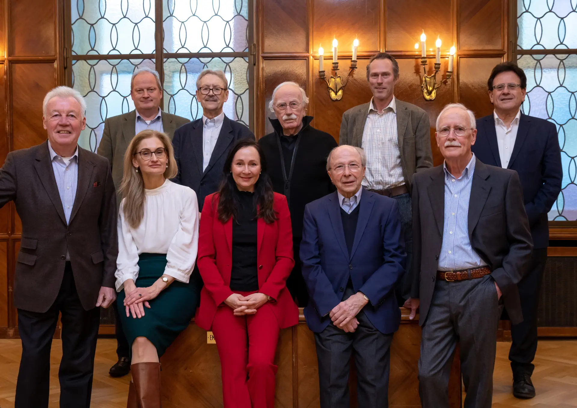 Gruppenfoto des Vorstands der Fördergesellschaft MiQua-Freunde. Acht Männer und zwei Frauen sitzen und stehen für das Gruppenfoto dicht beieinander. Die hintere Reihe steht, die vordere Reihe sitzt. Im Hintergrund leuchtet warmes Licht.