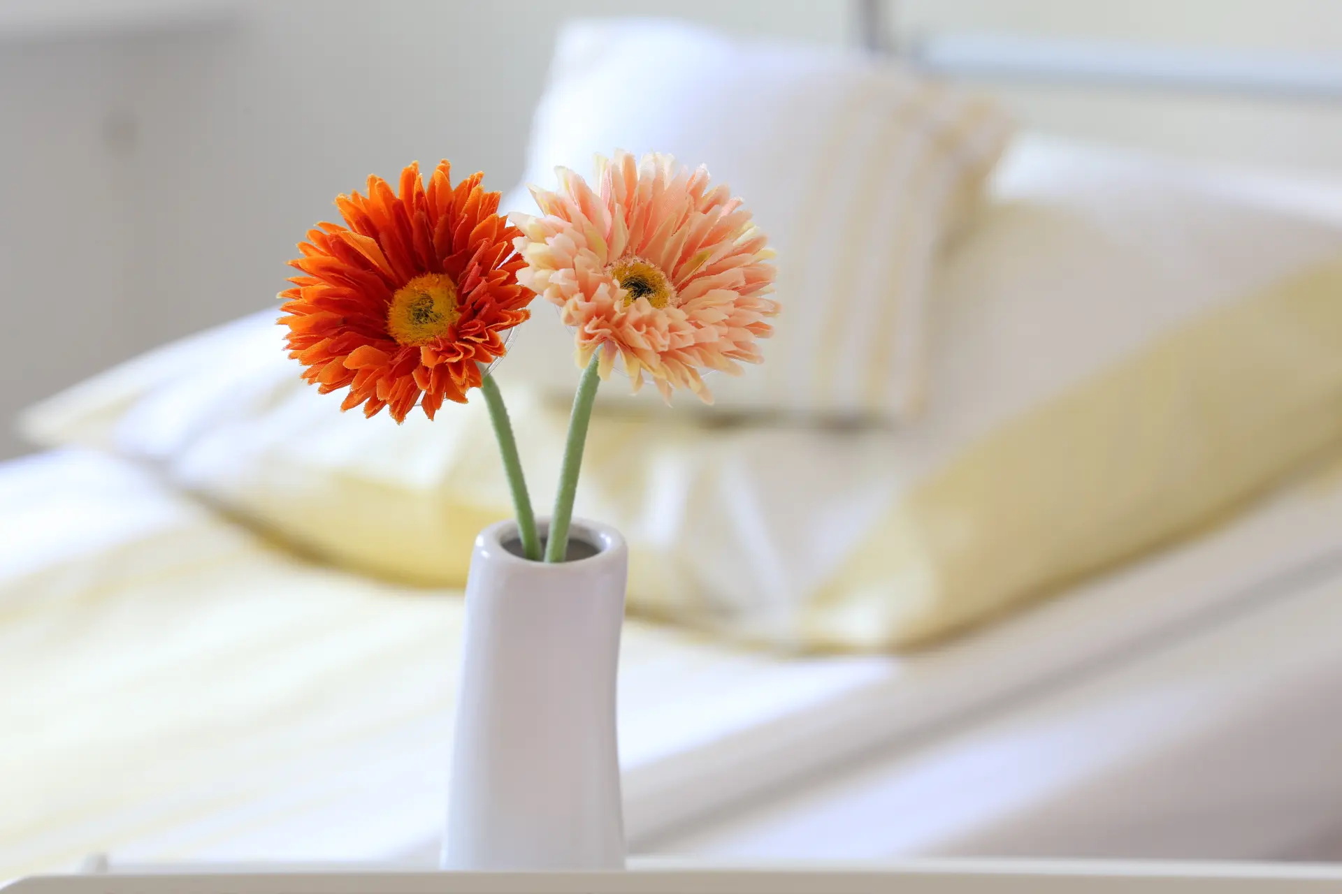 Bett mit gelber Bettwäsche und einer Blume auf dem Tisch