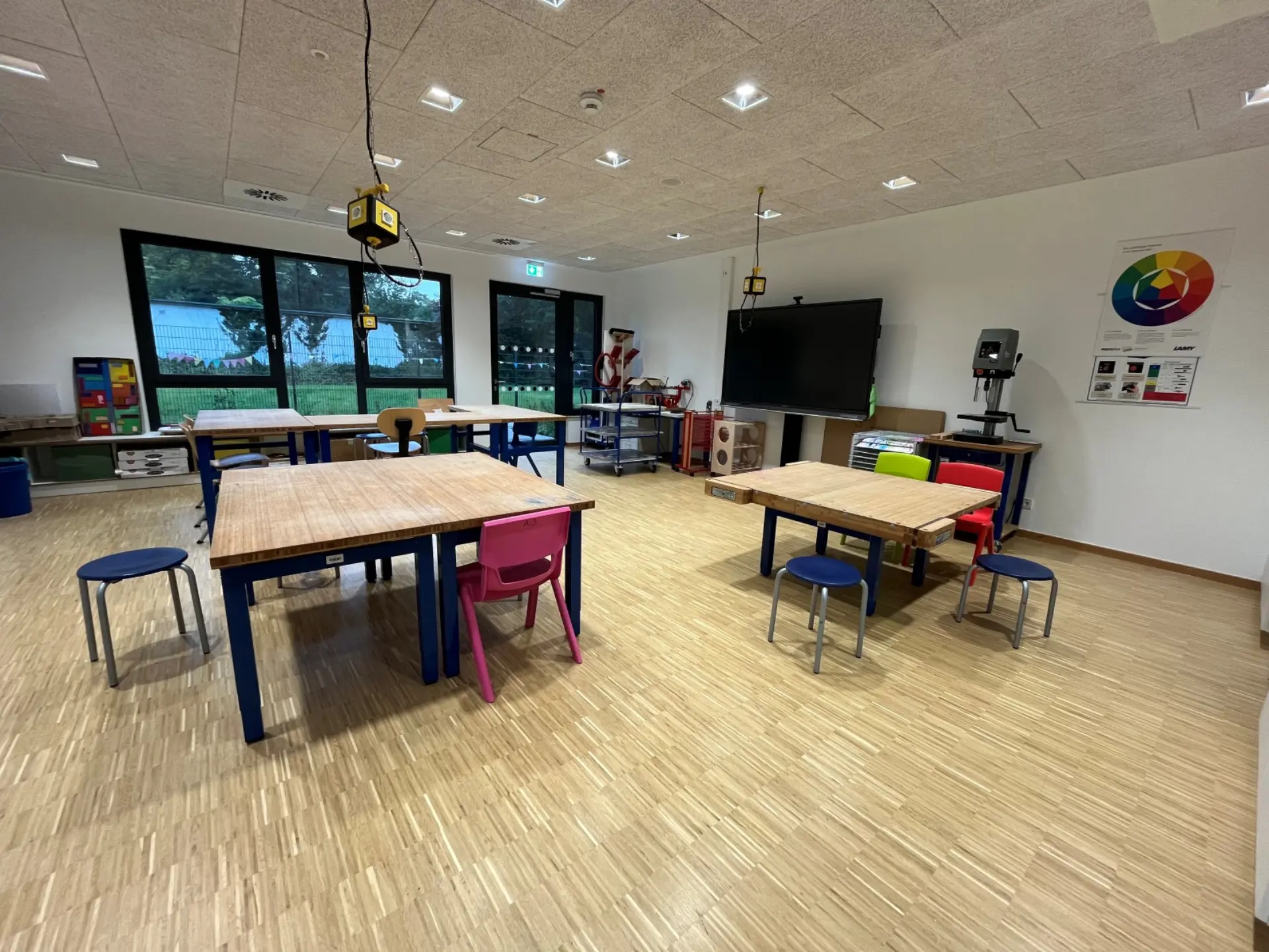 Ein Werken- oder Kunstraum: von der Decken hängen Steckdosen über Tischen mit dicken Holzplatten, eine Bohrmaschine und weitere Werkzeuge stehen an der Wand.