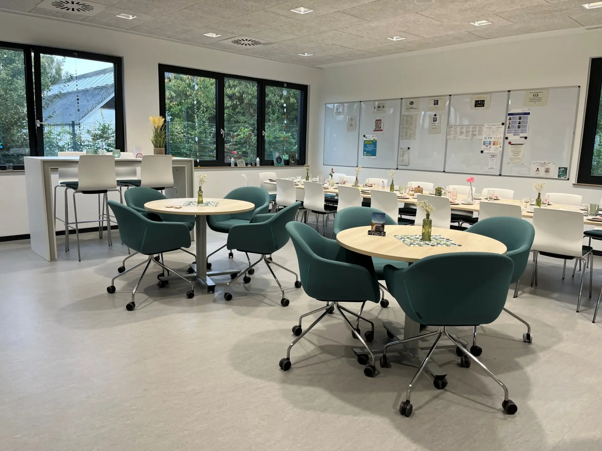 Moderner Besprechungsraum mit runden Tischen, Sesseln, hinten eine lange, eingedeckte Tafel und vier Whiteboards an der Wand