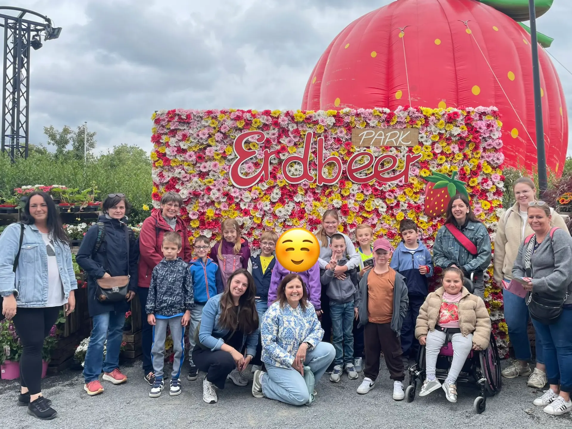 Gruppenfoto der Schildkröten und ihrer Begleitpersonen vor einer blütenverzierten Wand, auf der Erdbeer-Park steht. Im Hintergrund eine riesige, luftgefüllte Erdbeere.