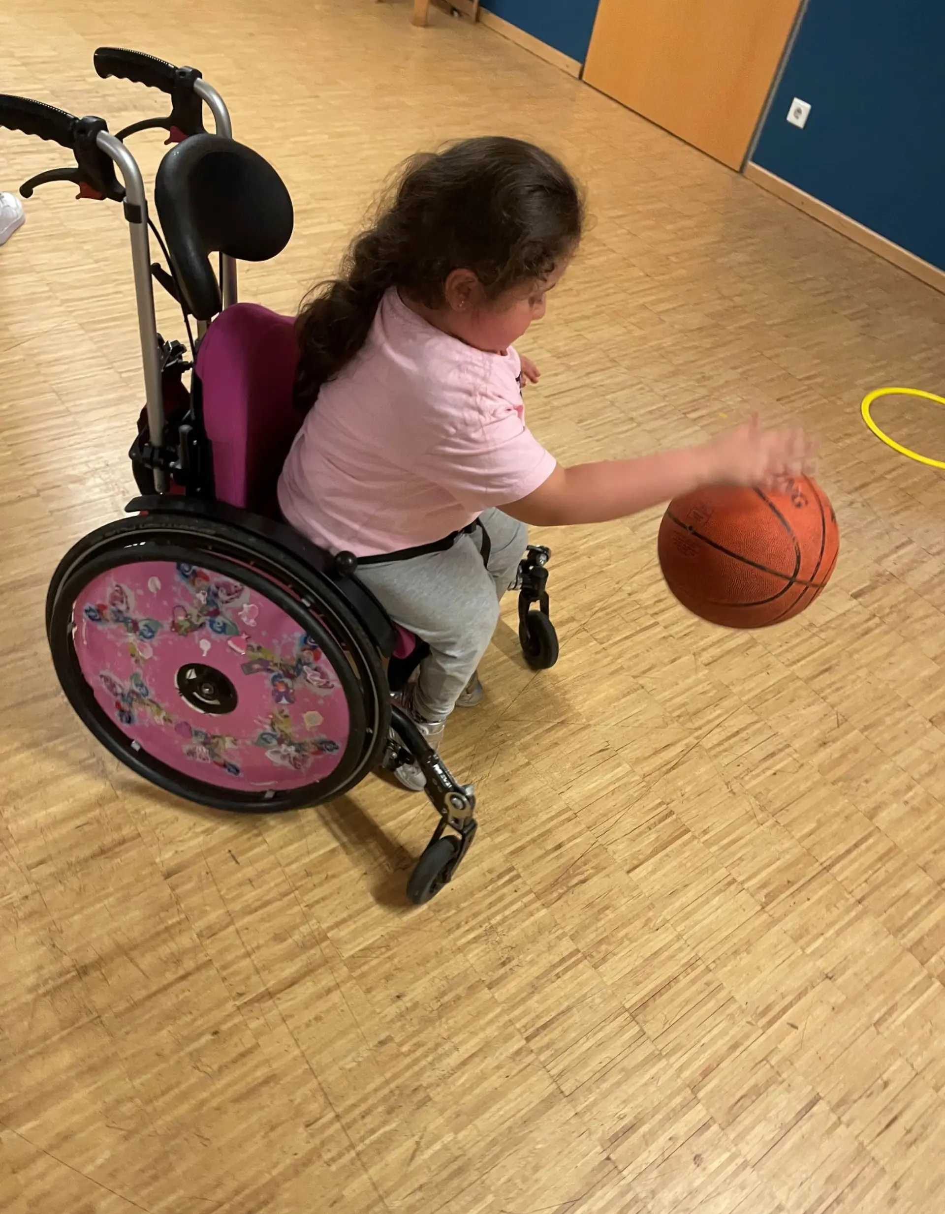 Ein Mädchen im Rollstuhl titscht einen Basketball in einer Turnhalle