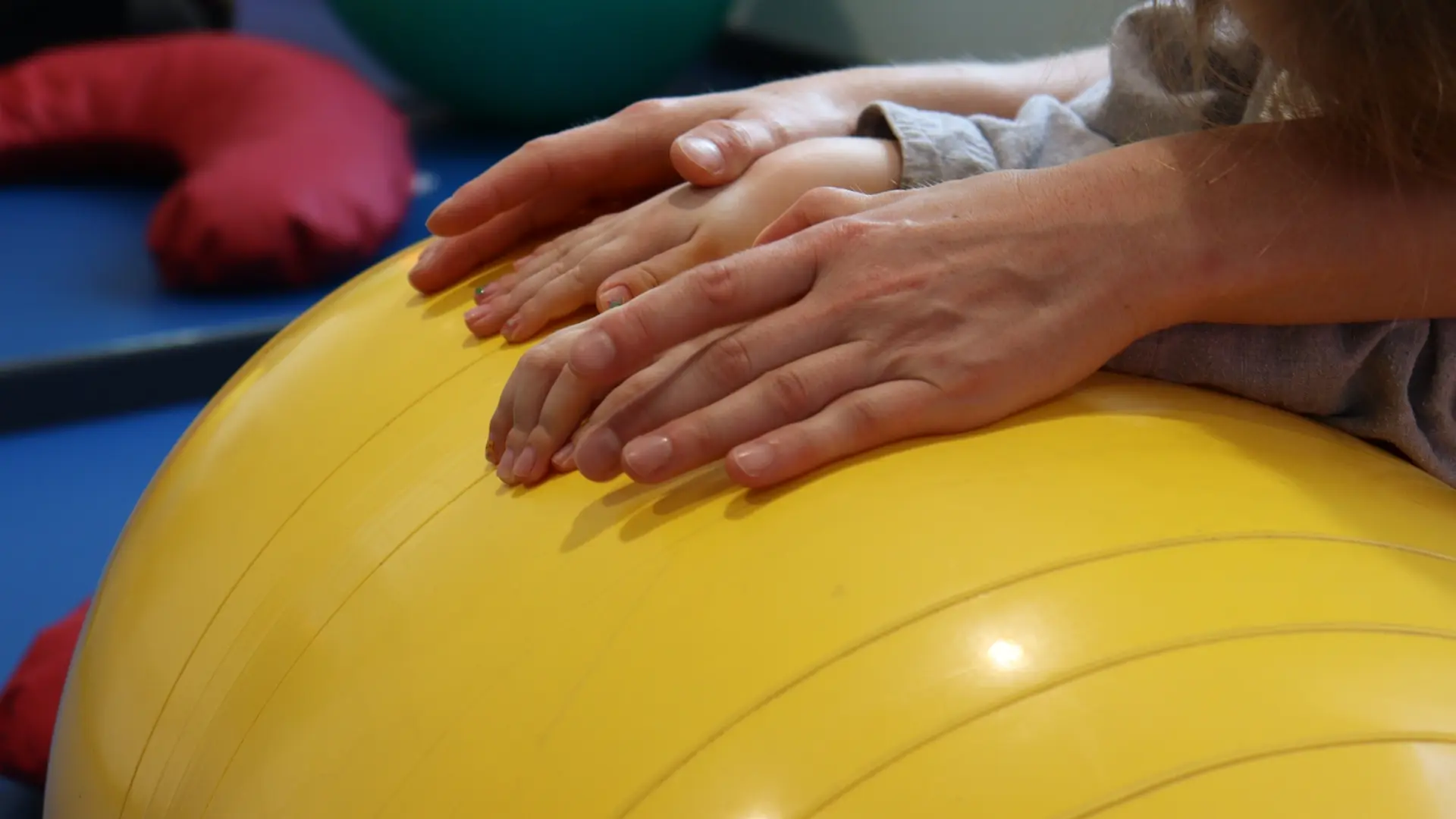 Erwachsenen- und Kinderhände auf einem gelbem Pezziball.