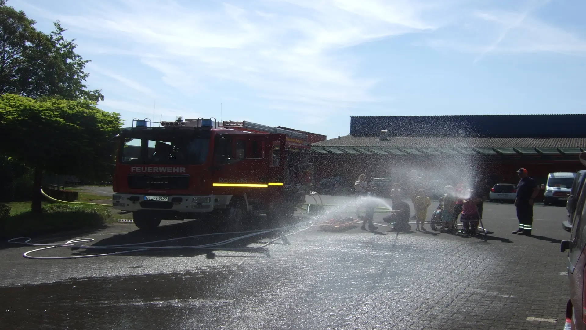 Die Schulklasse mit zwei Feuerwehrmännern mit Wasser spritzend vor dem Löschfahrzeug.