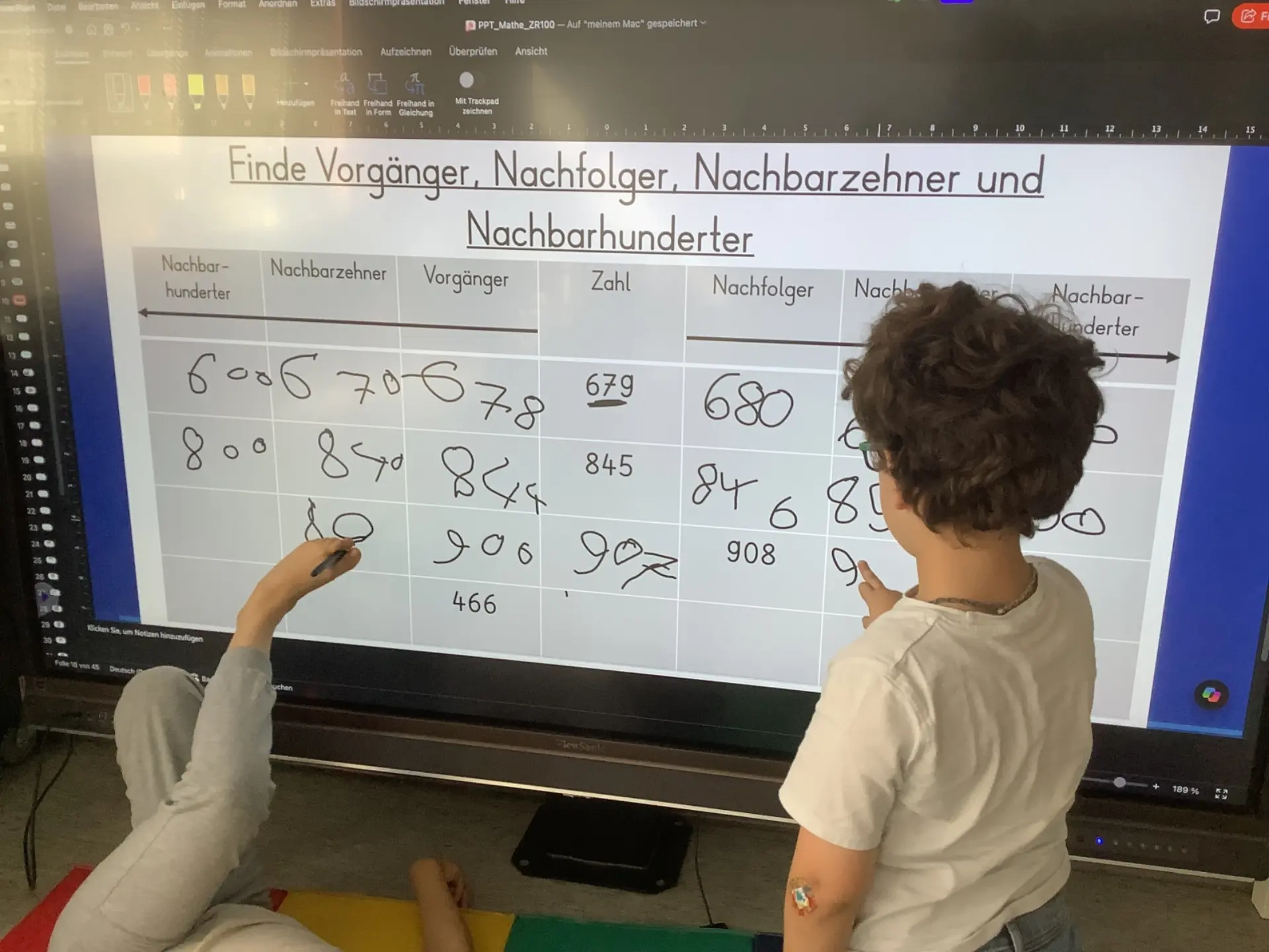 Zwei Kinder lösen Rechenaufgaben an digitaler Tafel