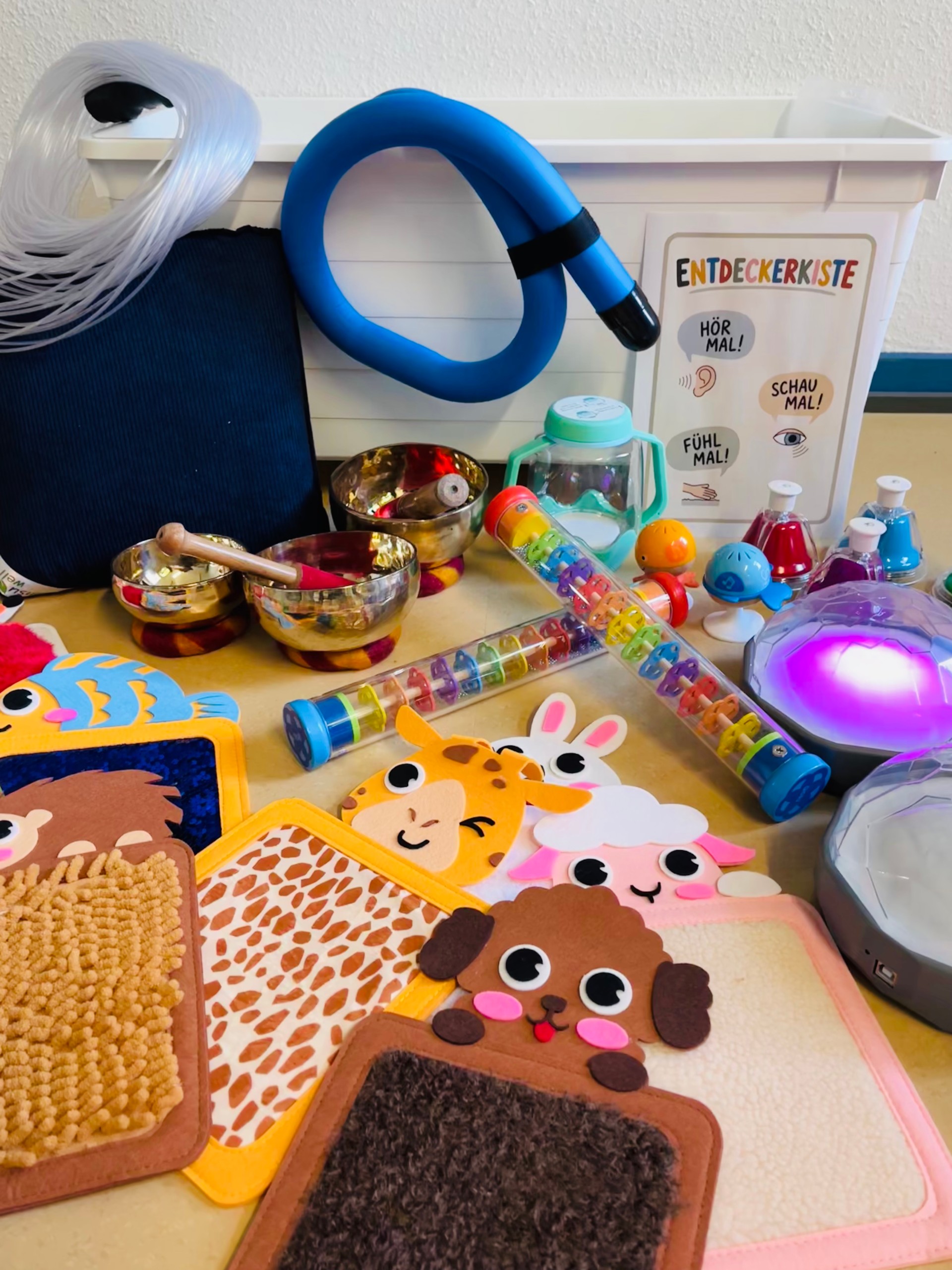 Ausstellungstische mit interkulturellen und religiösen Objekten wie Klangschalen, Instrumenten und Symbolen vor einer Holzwand zur Veranschaulichung der Projektarbeit an der Schule.