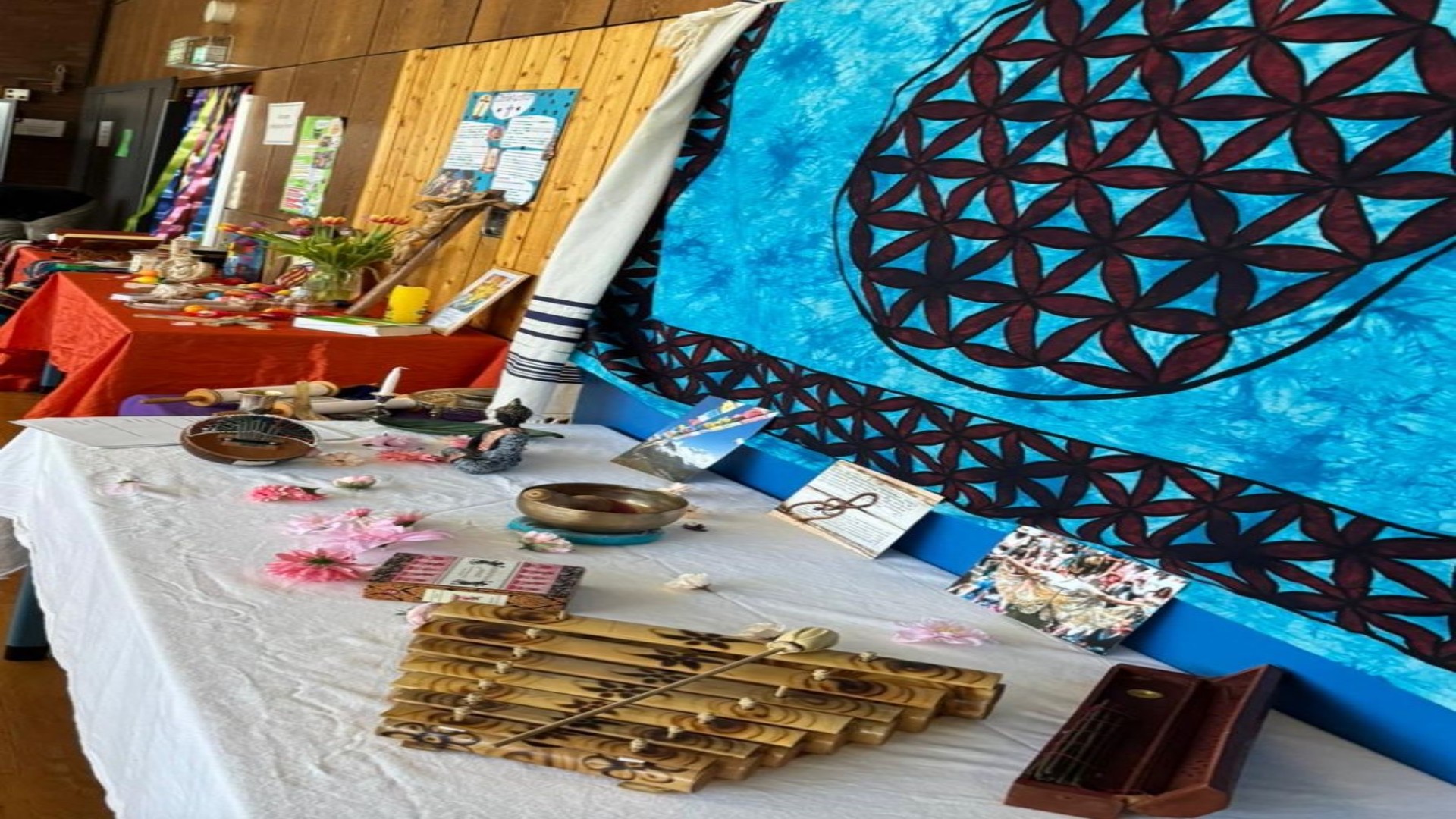 Ausstellungstische mit interkulturellen und religiösen Objekten wie Klangschalen, Instrumenten und Symbolen vor einer Holzwand zur Veranschaulichung der Projektarbeit an der Schule.