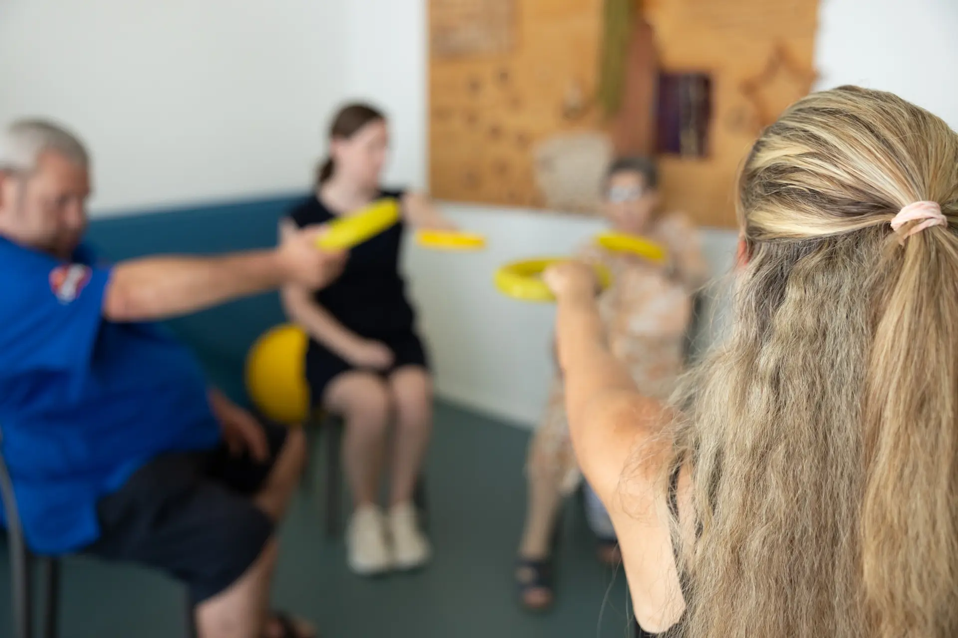 Gruppe von Menschen sitzt im Kreis und hält gelbe Stäbe nach vorne ausgestreckt