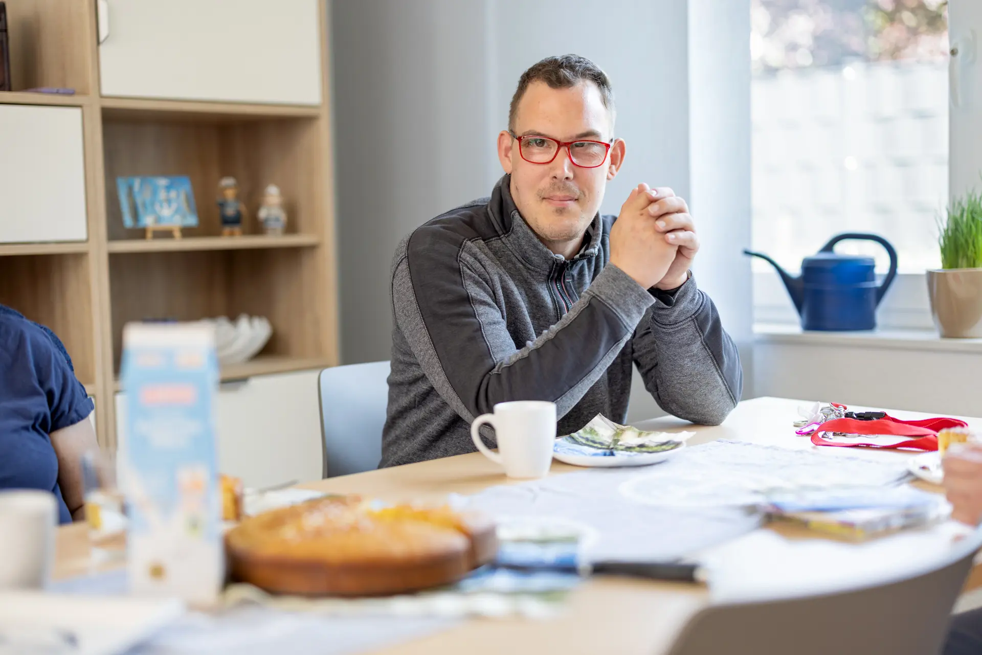 Mann mit roter Brille sitzt an gedecktem Tisch und schaut lächelnd zur Seite