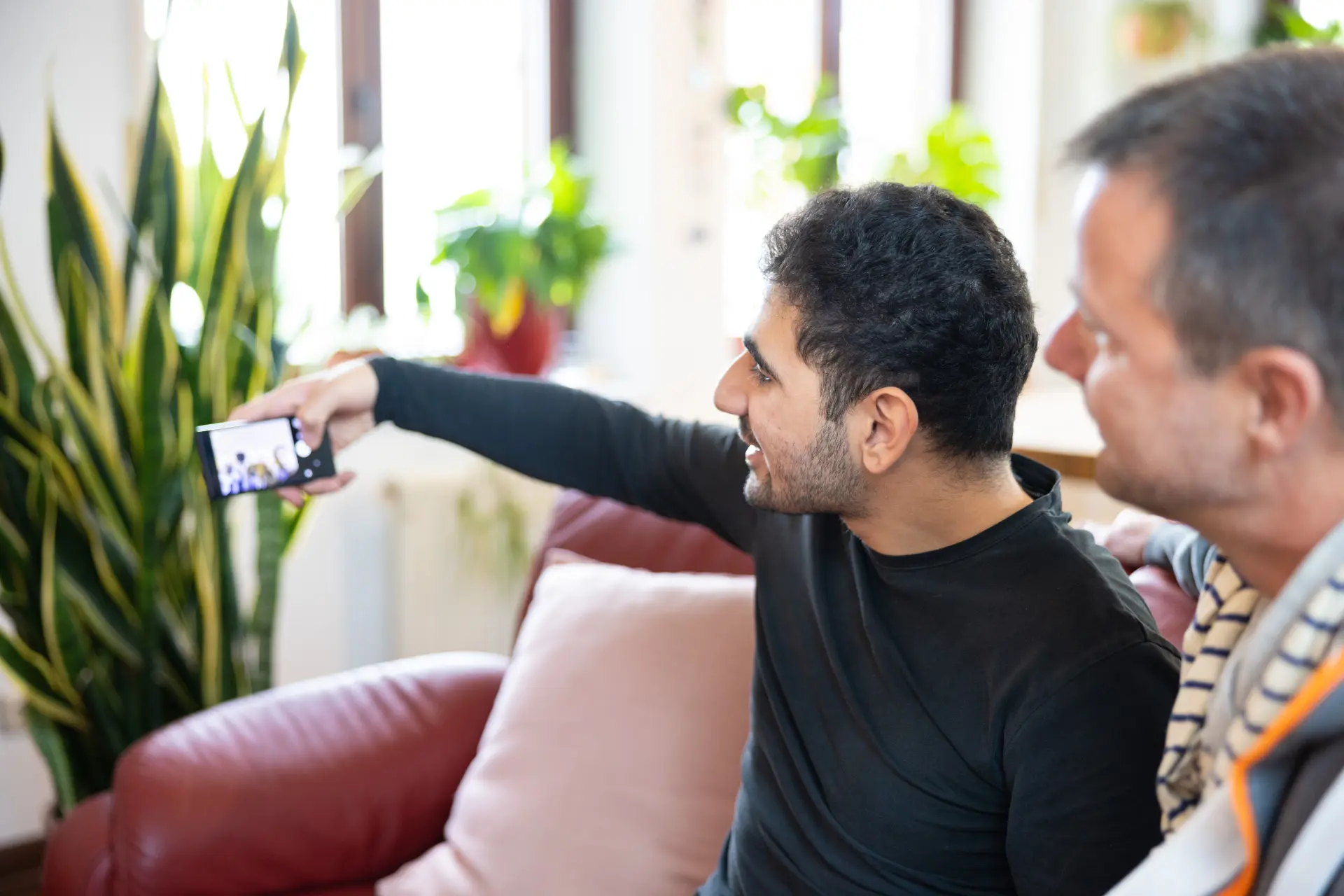 Zwei Männer sitzen auf einem Sofa, einer hält ein Smartphone und macht ein Selfie