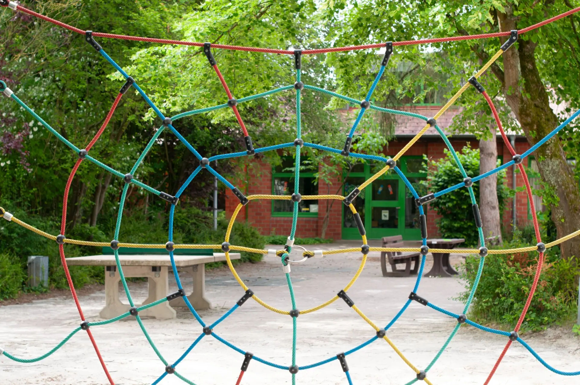 Buntes Kletternetz auf dem Schulhof mit Tischtennisplatte und Schulgebäude im Hintergrund