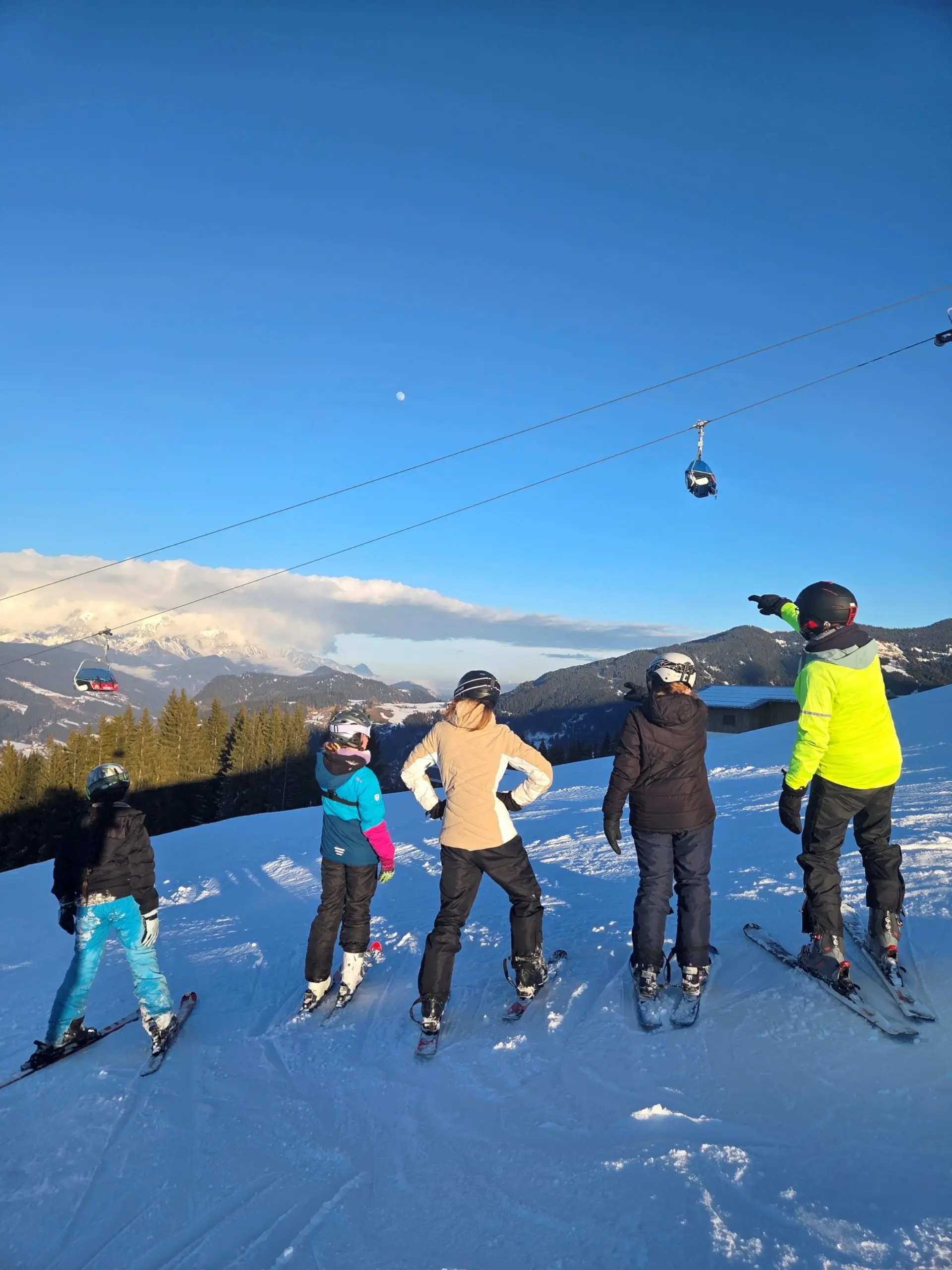 Schüler*innen mit Skianzügen und Ski stehen im Schnee und schauen zum Lift in der Nähe.