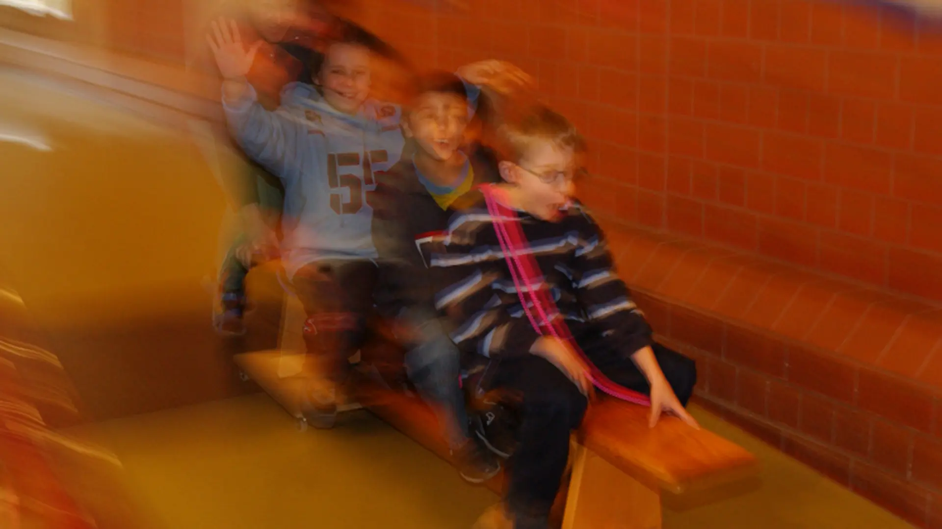 Ein verwischtes Bild von vier Schüler*innen, die mit einem Holzauto rutschen und viel Spaß dabei haben.
