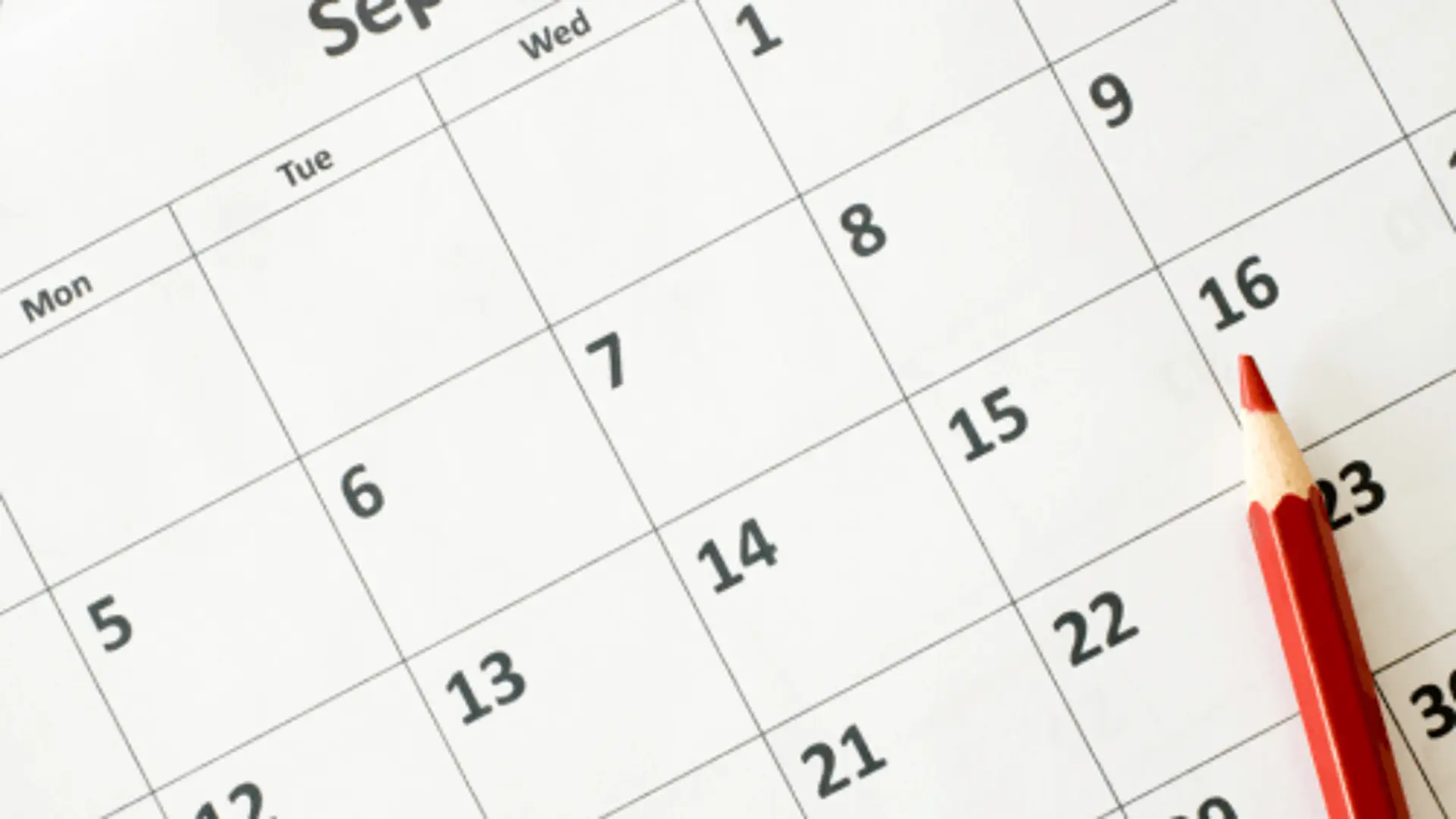 Eine Nahaufnahme von einem Papierkalender mit Kästchen für jeden Tag. Darauf liegt ein Bleistift.