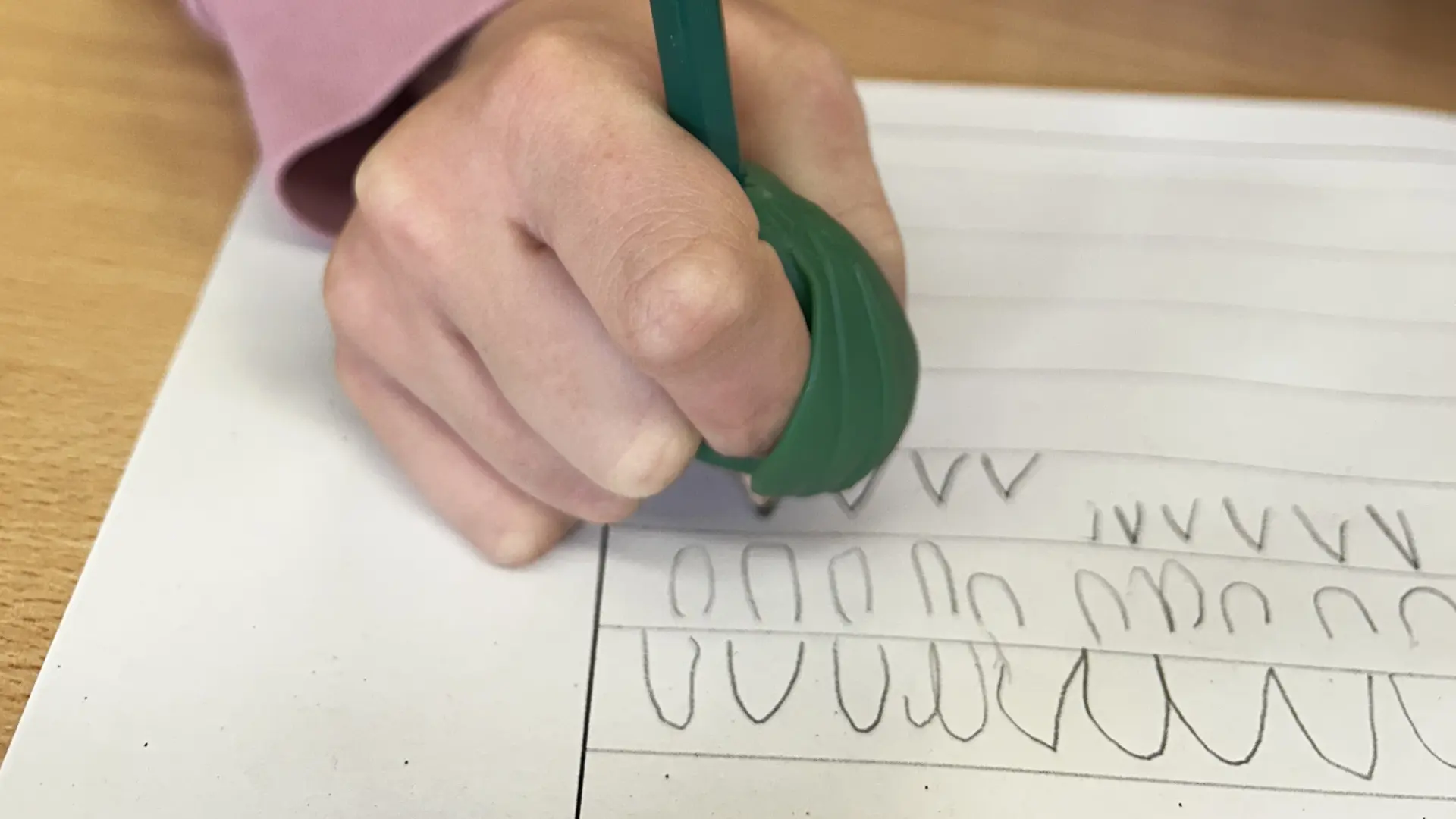 Ein Kind übt schreiben mit einem Bleistift und einem speziellen Gummiaufsatz für den Finger und mehr Stabilität.