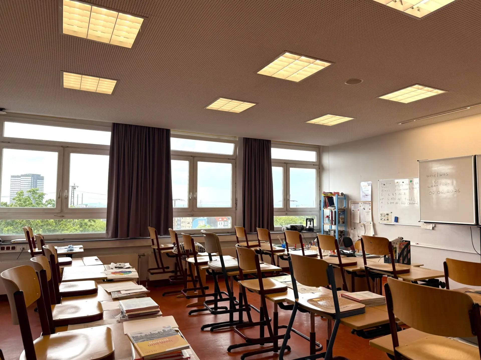 Heller Klassenraum mit vielen Holztischen und -stühlen sowie einer digitalen Tafel und einem Whiteboard.