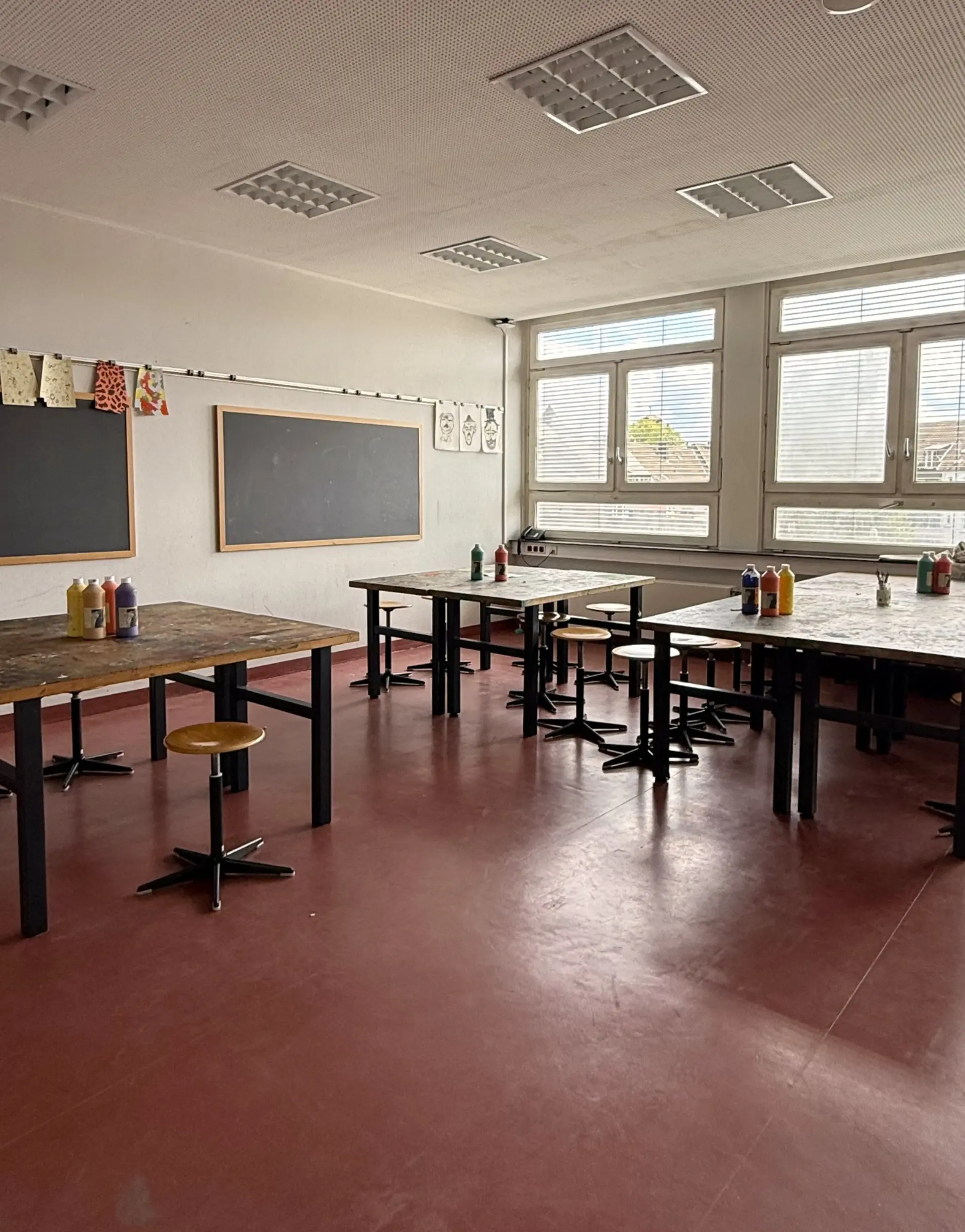 Weitläufiger, heller Kunstraum mit großen Holztischen und zwei Kreidetafeln an der Wand