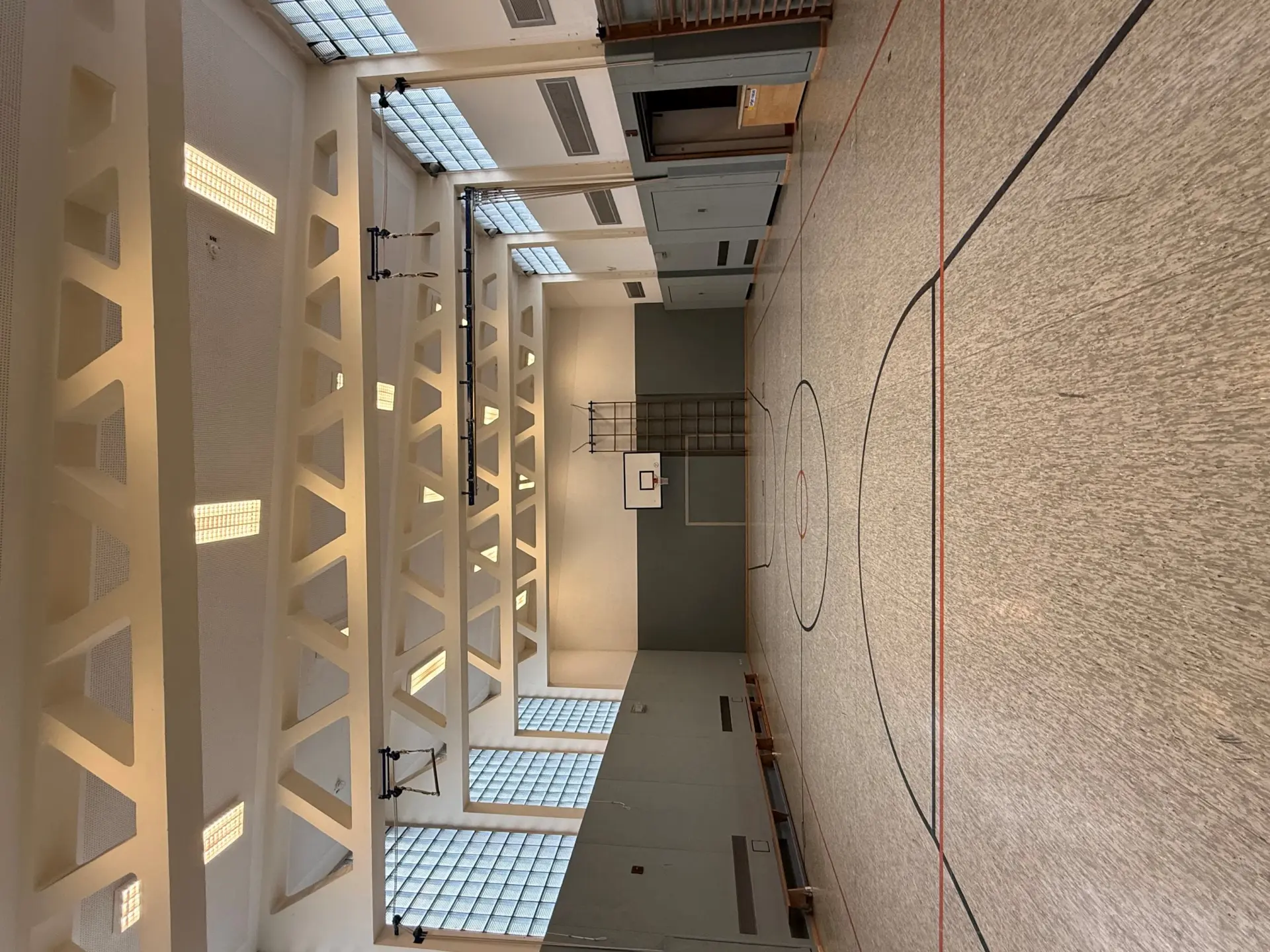 Die helle und weitläufige Sporthalle mit markiertem Spielfeld, Basketballkorb und Sprossenwand für den Sportunterricht.
