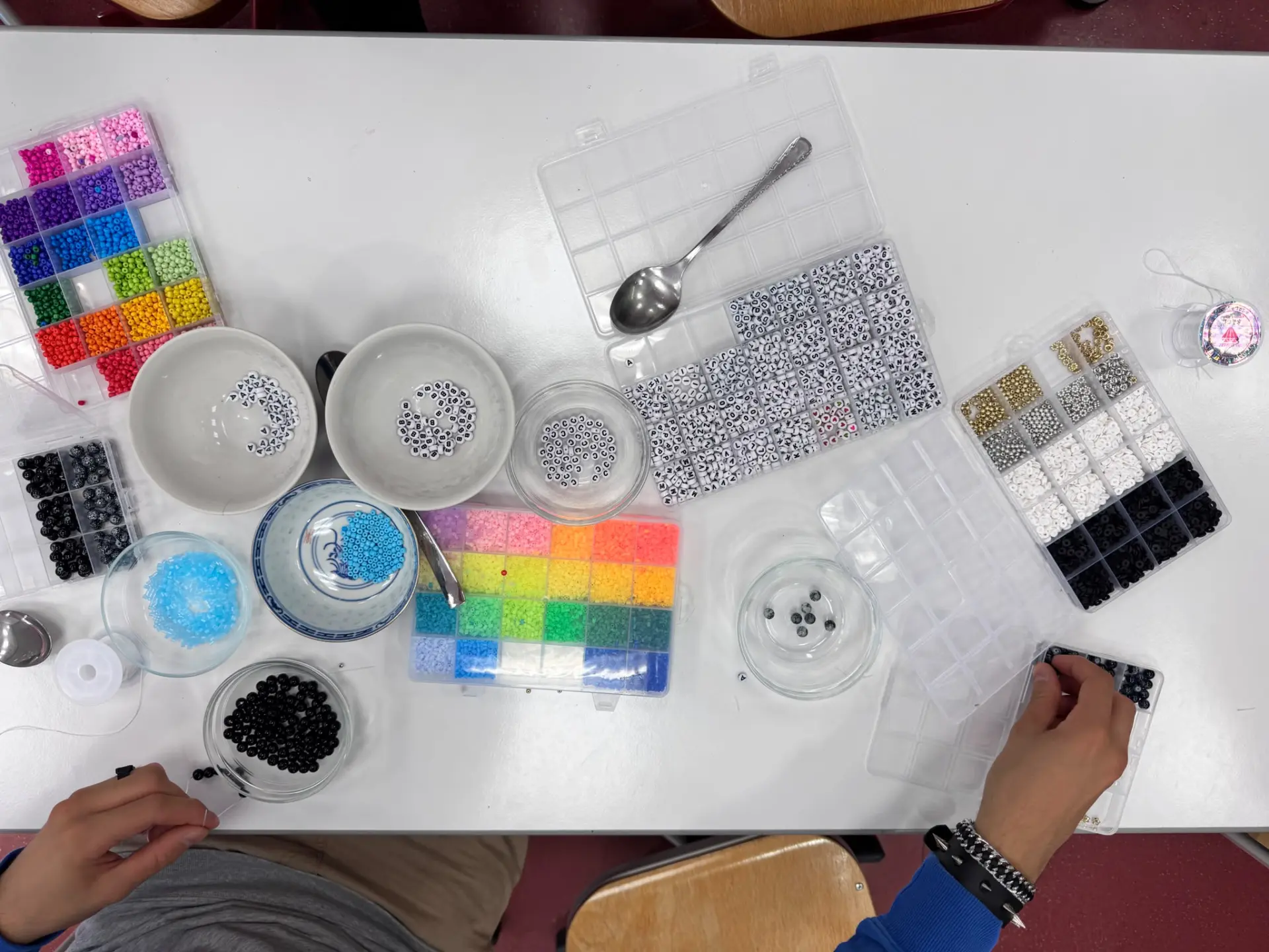Ein weitläufiger Platz vor dem Schulgebäude der LVR-Wilhelm-Körber-Schule. Überall sind Kinder, Jugendliche und Erwachsene zu sehen. In der Mitte spielen neun Schüler*innen ein Spiel mit Seilen und Holzblöcken.