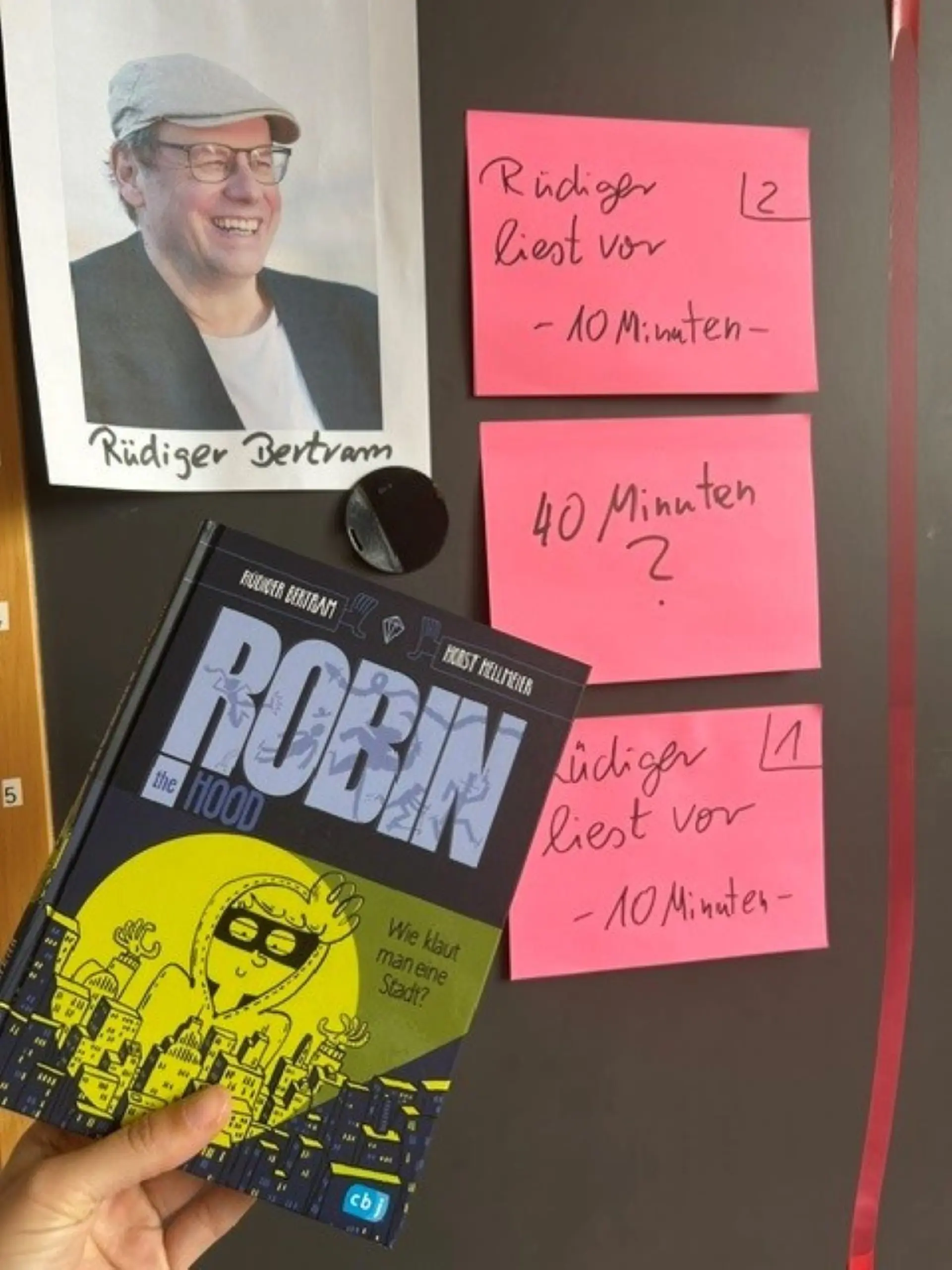 Buch "Robin the Hood", ein Porträt von Rüdiger Bertram und rosa Zettel mit dem Zeitplan für die Autorenlesung