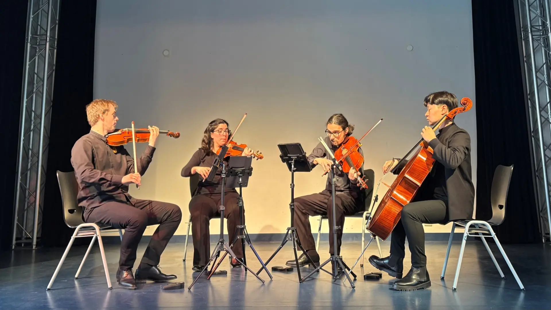 Vier Musiker*innen mit Streichinstrumenten spielen auf der Bühne in der Schulaula.