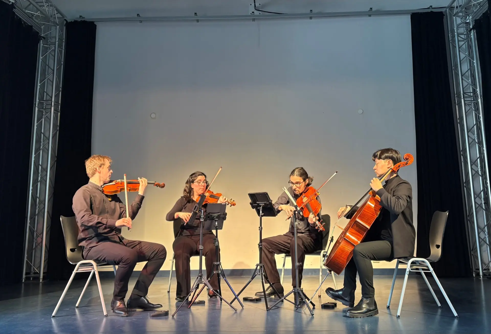 Vier Musiker*innen mit Streichinstrumenten spielen auf der Bühne in der Schulaula.