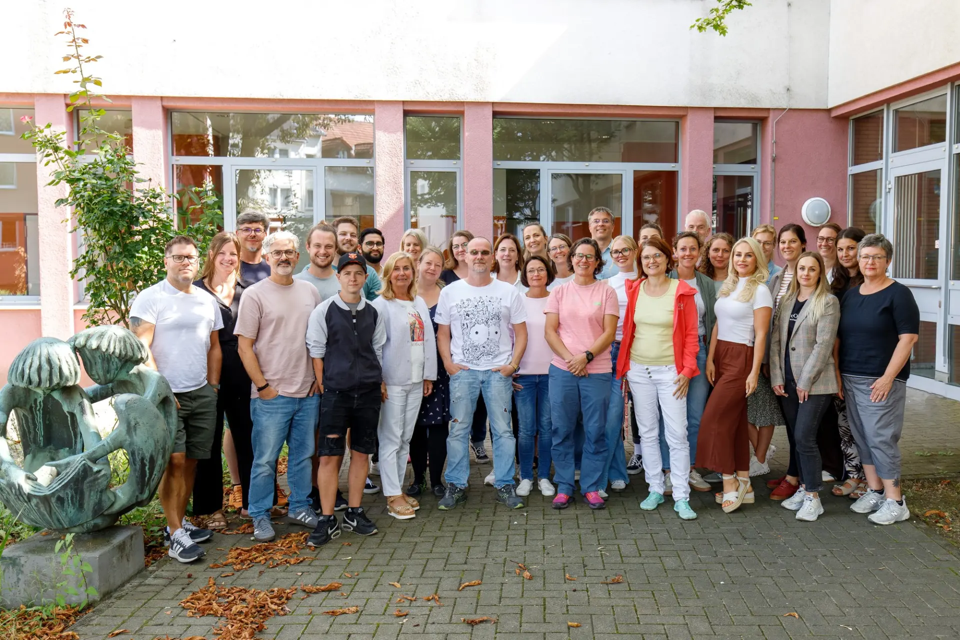 Ein Gruppenporträt von mehreren Personen, die das Schulkollegium der LVR-Wilhelm-Körber-Schule bilden. Sie wurden an einem sonnigen Tag vor dem Schulgebäude fotografiert.