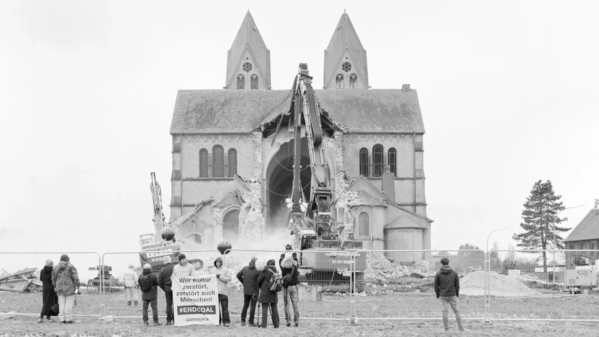 Menschen mit Plakaten stehen vor einer Kirche, die abgerissen wird.