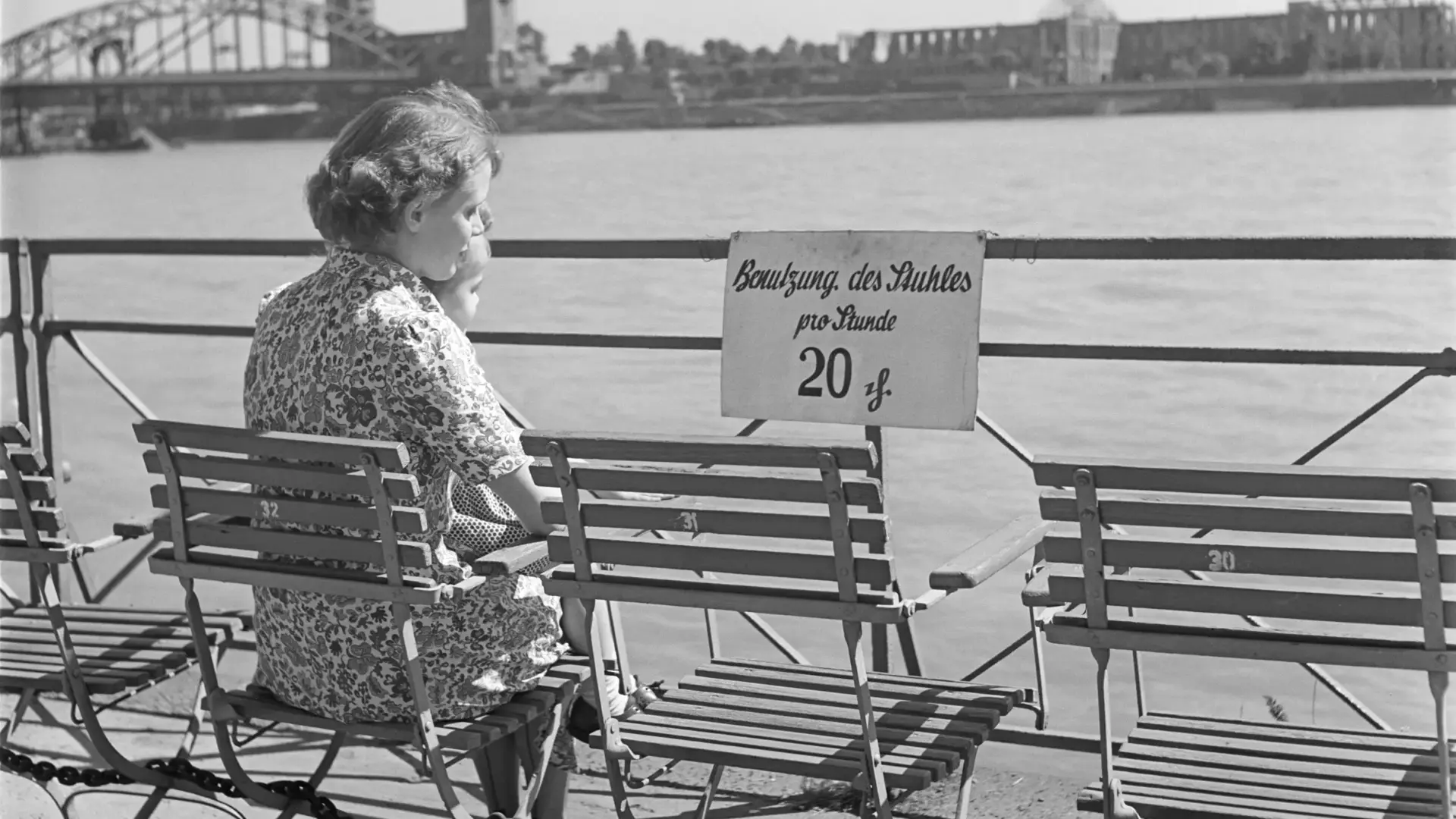 Eine Frau und ein Mädchen sitzen auf einer Bank am Flussufer.