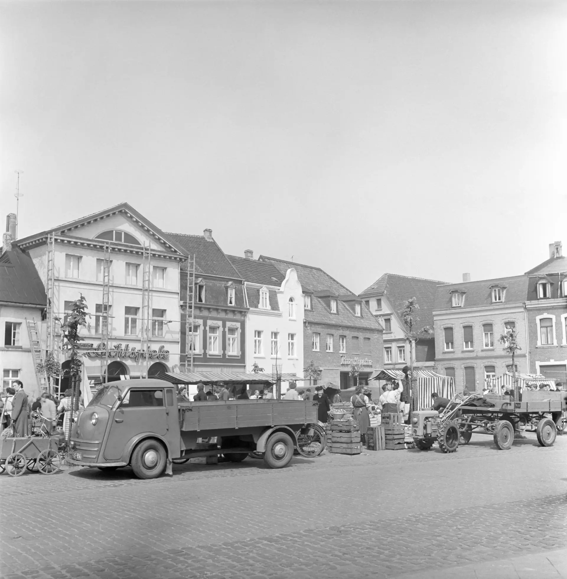 Ein Platz mit Marktständen und einem Lieferwagen im Vordergrund.