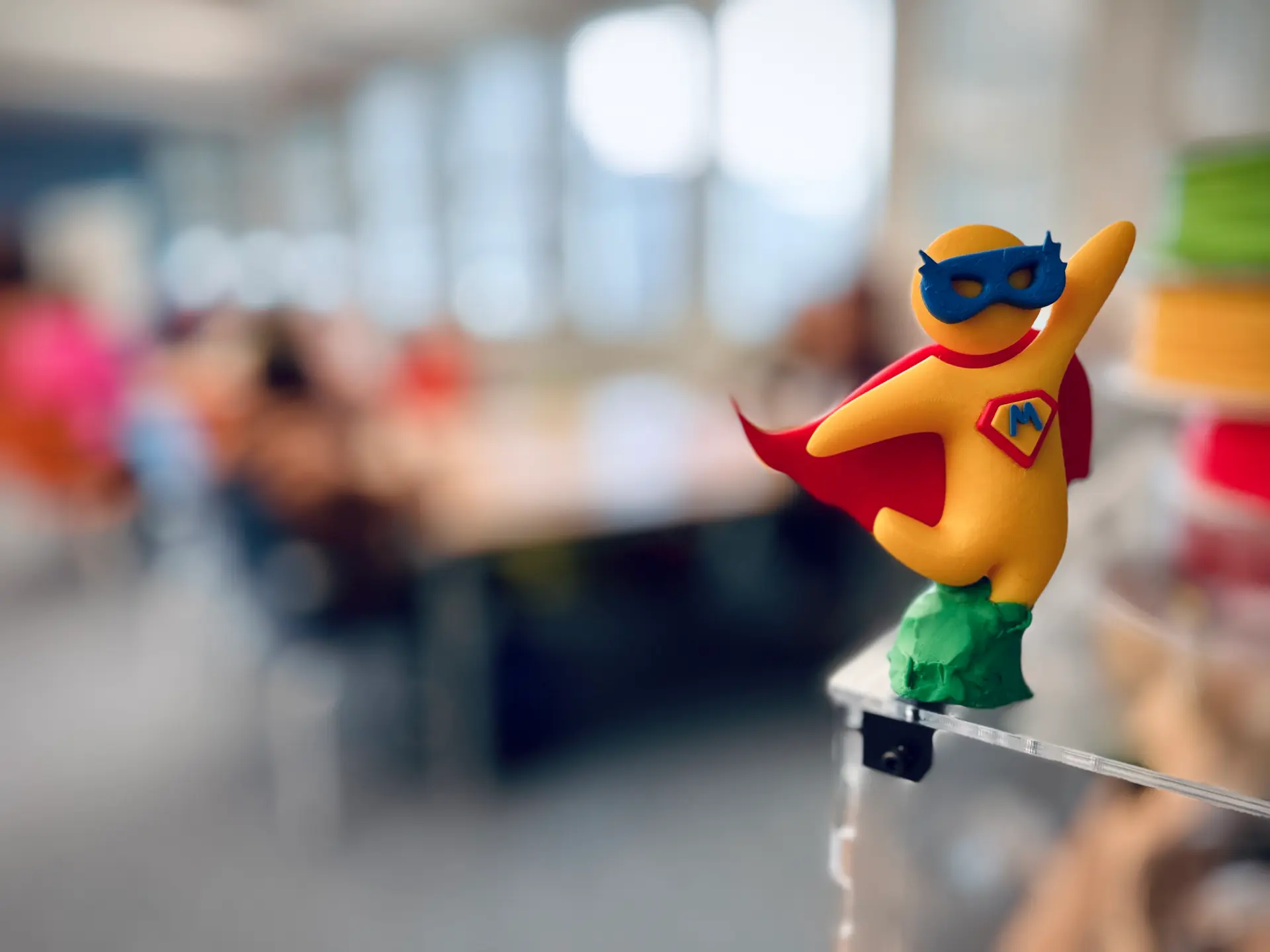 Im Vordergrund die kleine Medienheld*innen-Figur, im Hintergrund verschwommen Menschen am Tisch.