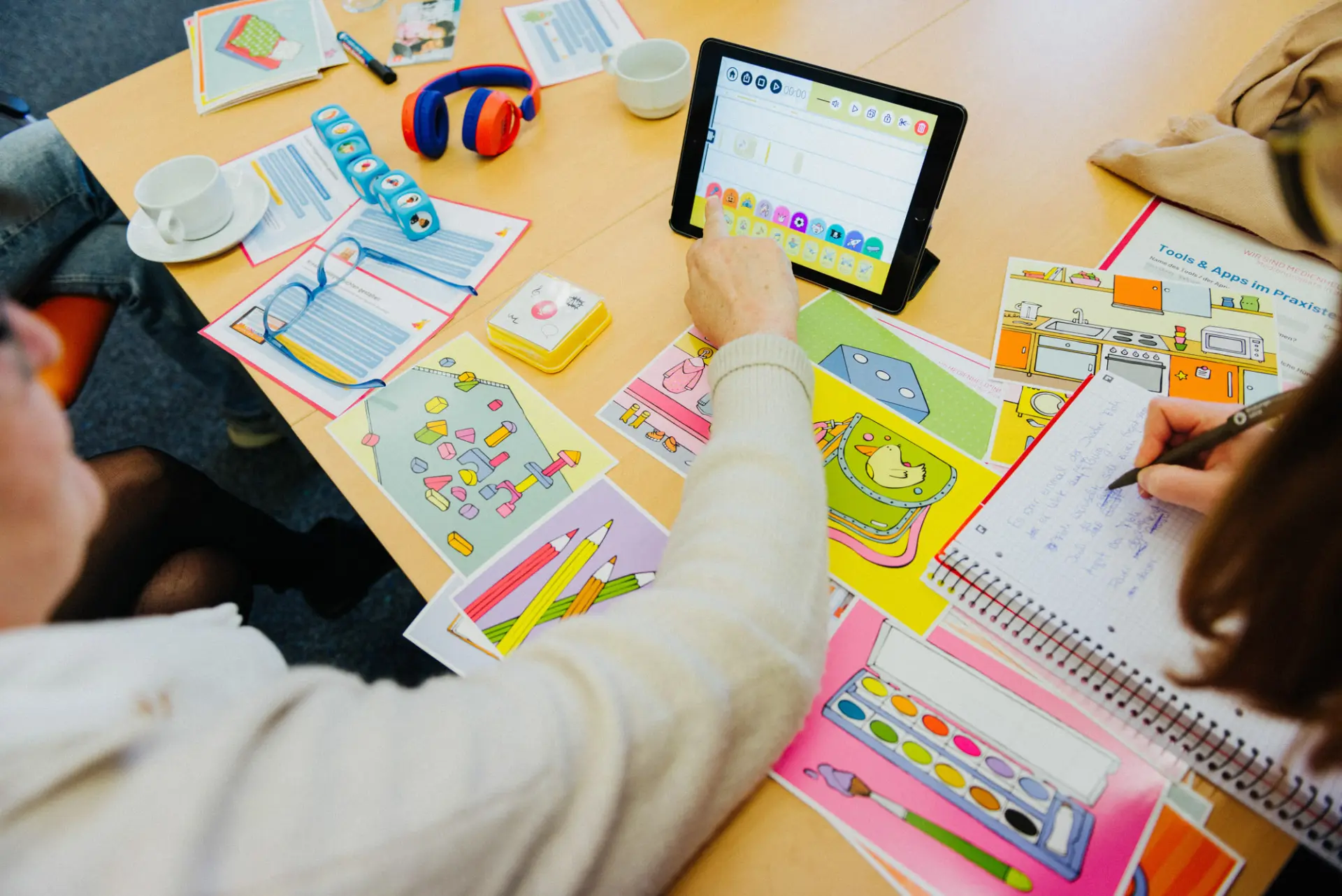 Auf dem Tisch liegen Materialien zum Thema hören, eine Hand klickt auf ein Ipad.